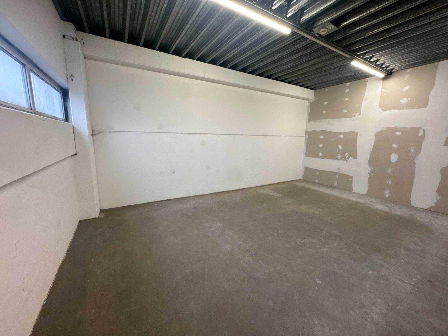 Kleiner Raum mit Betonboden, einem Fenster und teilweise unverputzten Wänden, ideal als Abstellraum.