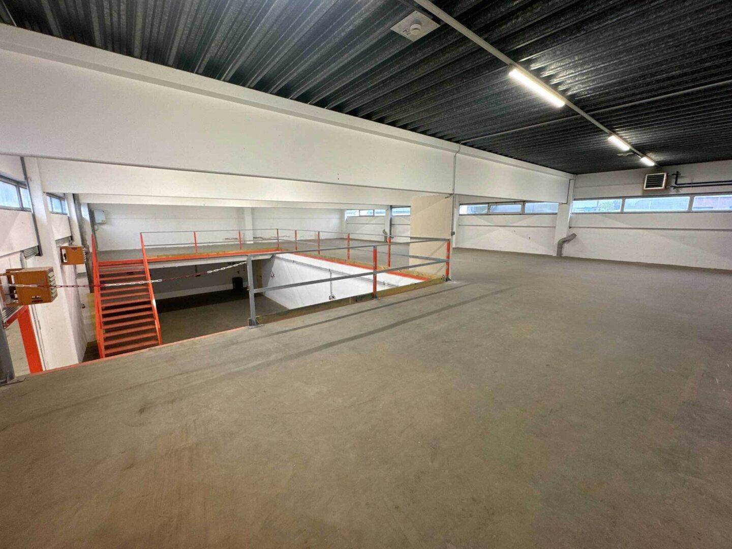 Weitläufige Empore mit Betonboden, niedrigen Fenstern und einer Rampe, die zum unteren Bereich führt.