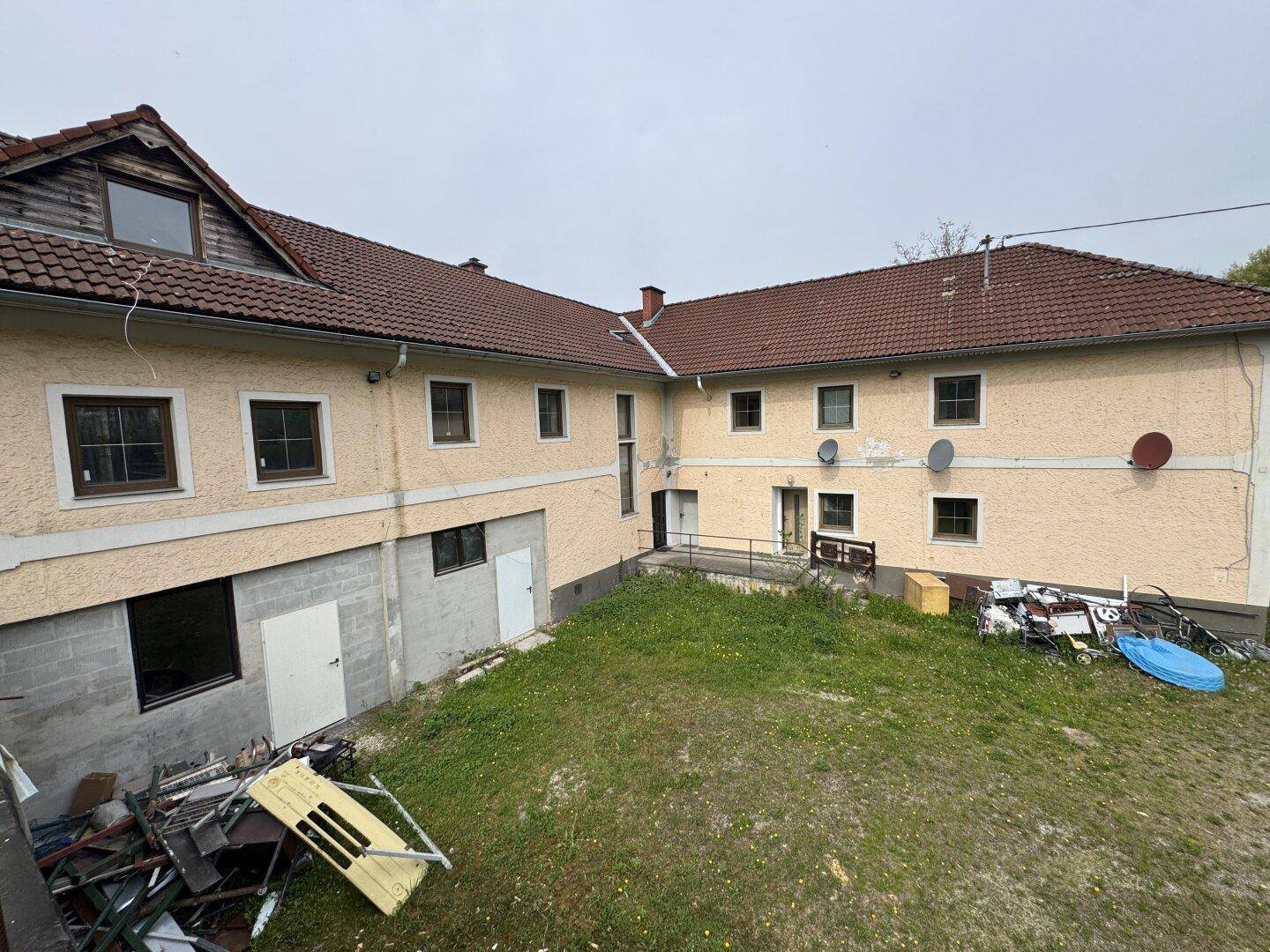 Rückseite eines Gebäudes mit mehreren Fenstern und einem ungepflegten Hinterhof.