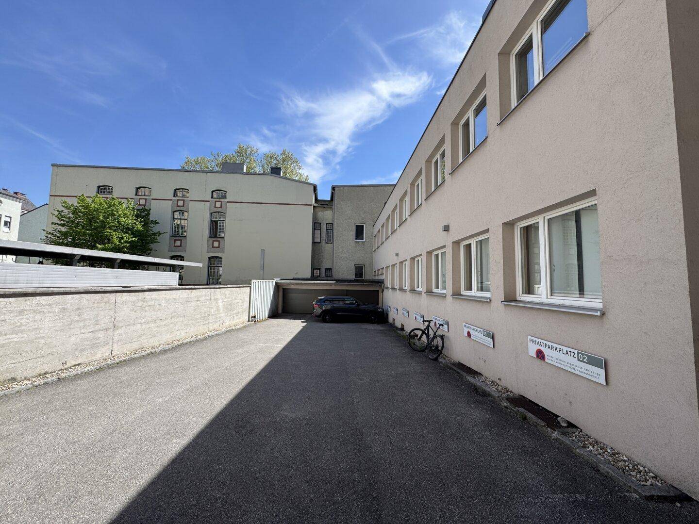 Außenansicht eines Gebäudes mit Zufahrt zu einem privaten Parkplatz und Garagen unter blauem Himmel.