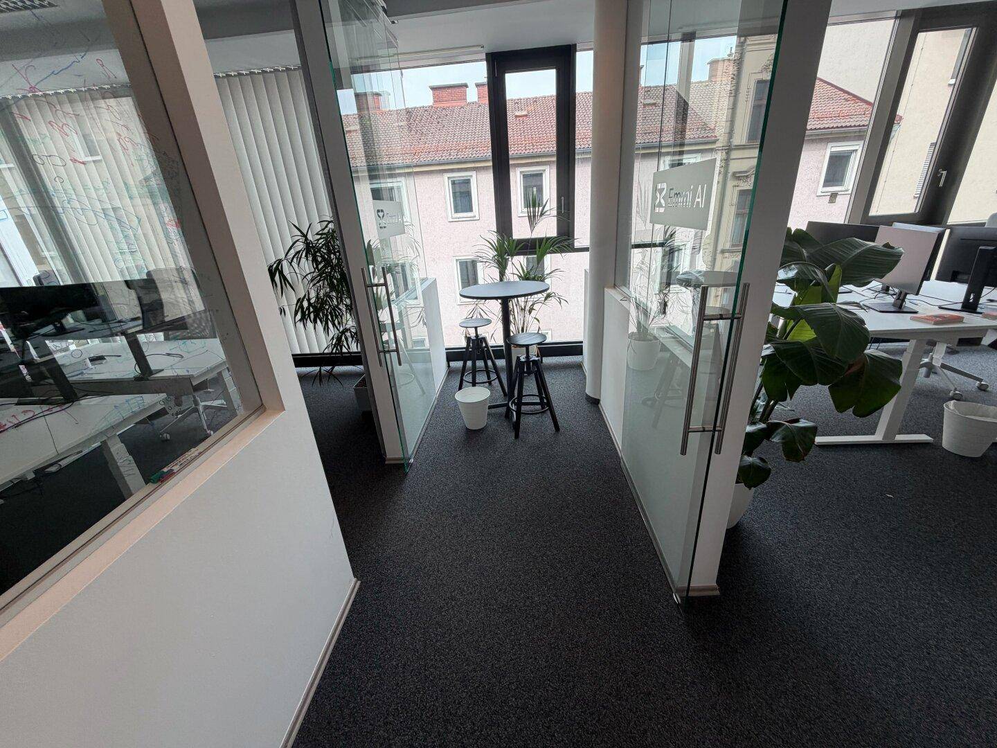 Bürobereich mit Glaswänden, Teppichboden und einem kleinen Stehtisch für kurze Besprechungen oder Pausen.