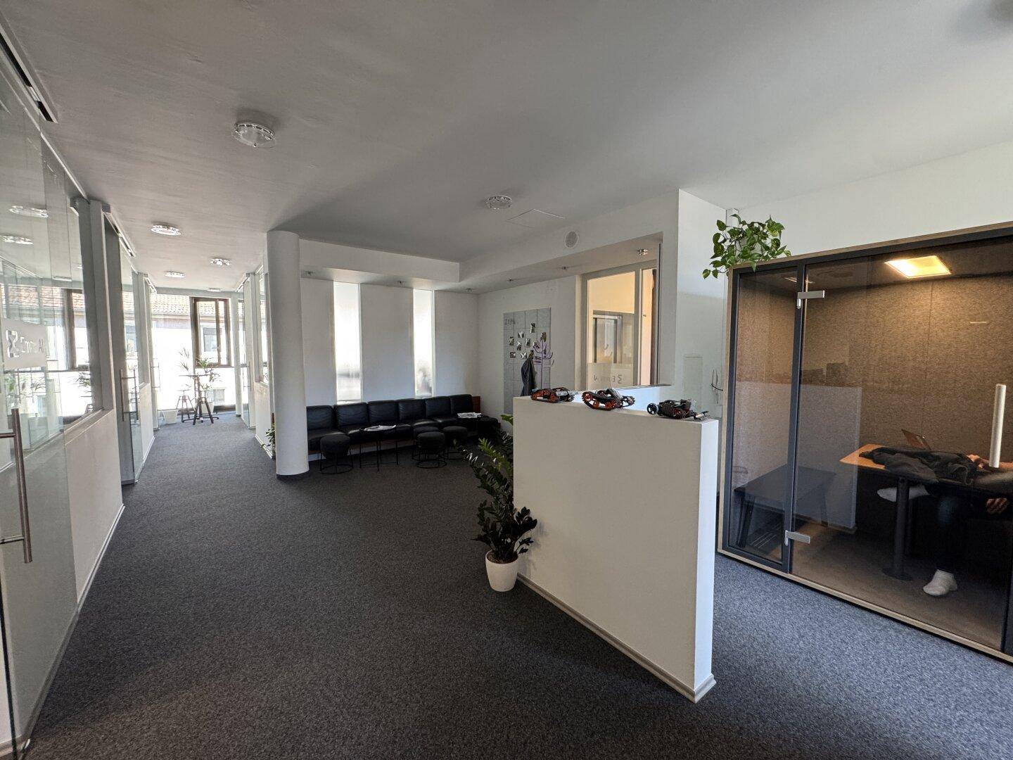 Moderner Bürobereich mit Wartezone, Glaswänden und einer schallgedämmten Telefonzelle für private Gespräche.