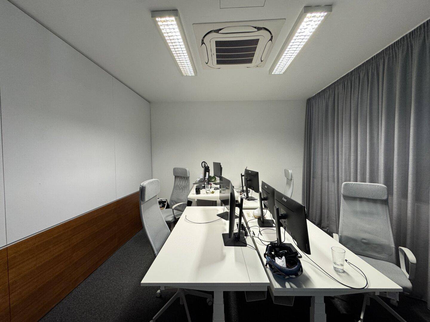 Helles Büro mit mehreren Arbeitsplätzen, Klimaanlage und Holzvertäfelung an einer Wand für eine warme Note.