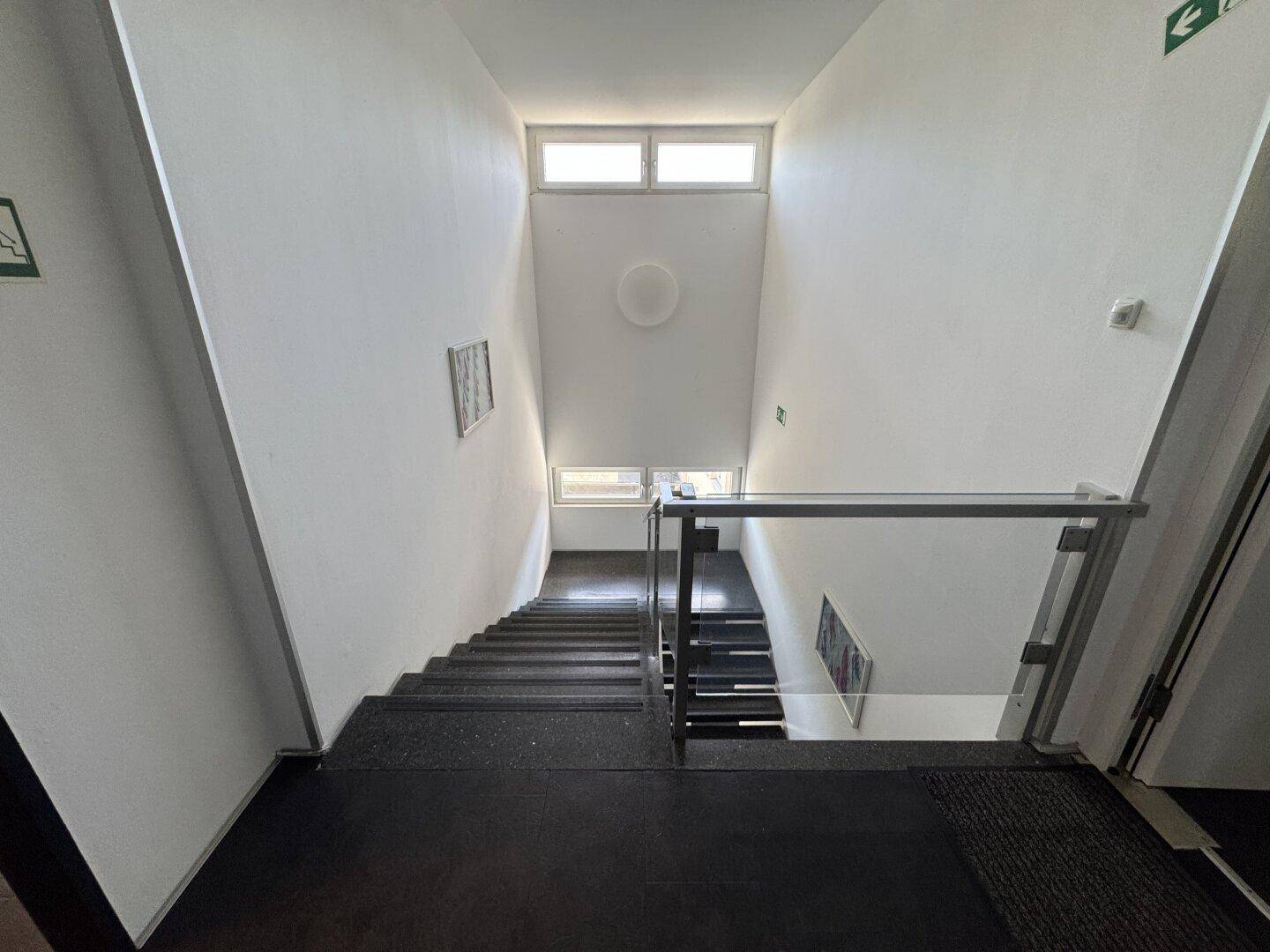 Helles Treppenhaus mit mehreren Etagen, Geländer und Fenstern, die für natürliches Tageslicht sorgen.