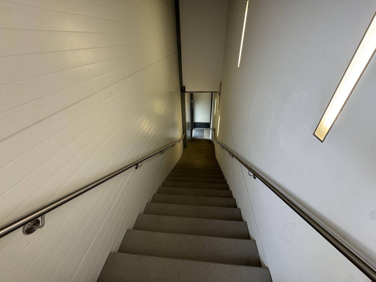 Moderner Treppenaufgang mit Edelstahlgeländer und indirekter Beleuchtung an den Wänden.