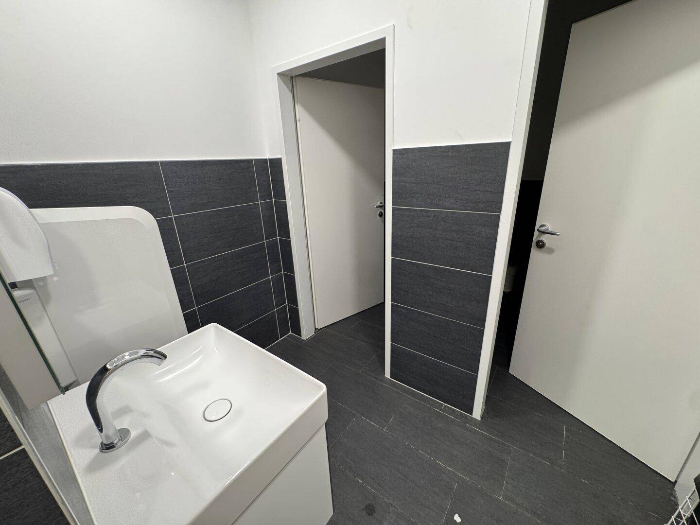 Modernes WC mit dunklen Fliesen an den Wänden und einem weißen Waschbecken.
