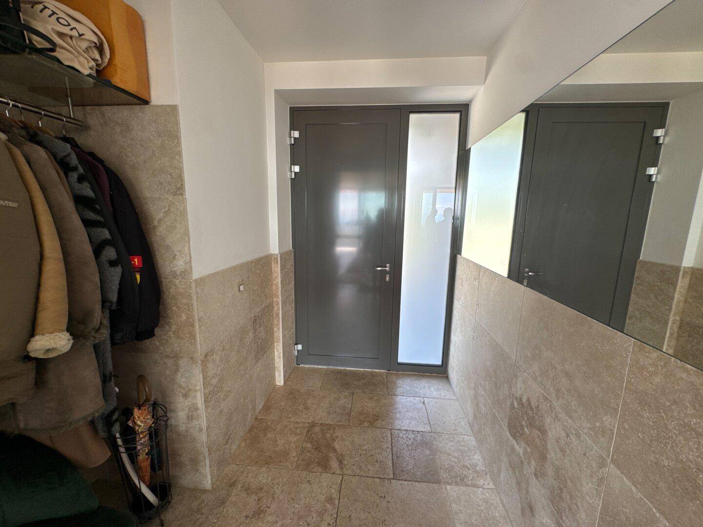 Heller Eingangsbereich mit Fliesenboden und einer Garderobe, die zum Wohnbereich führt.