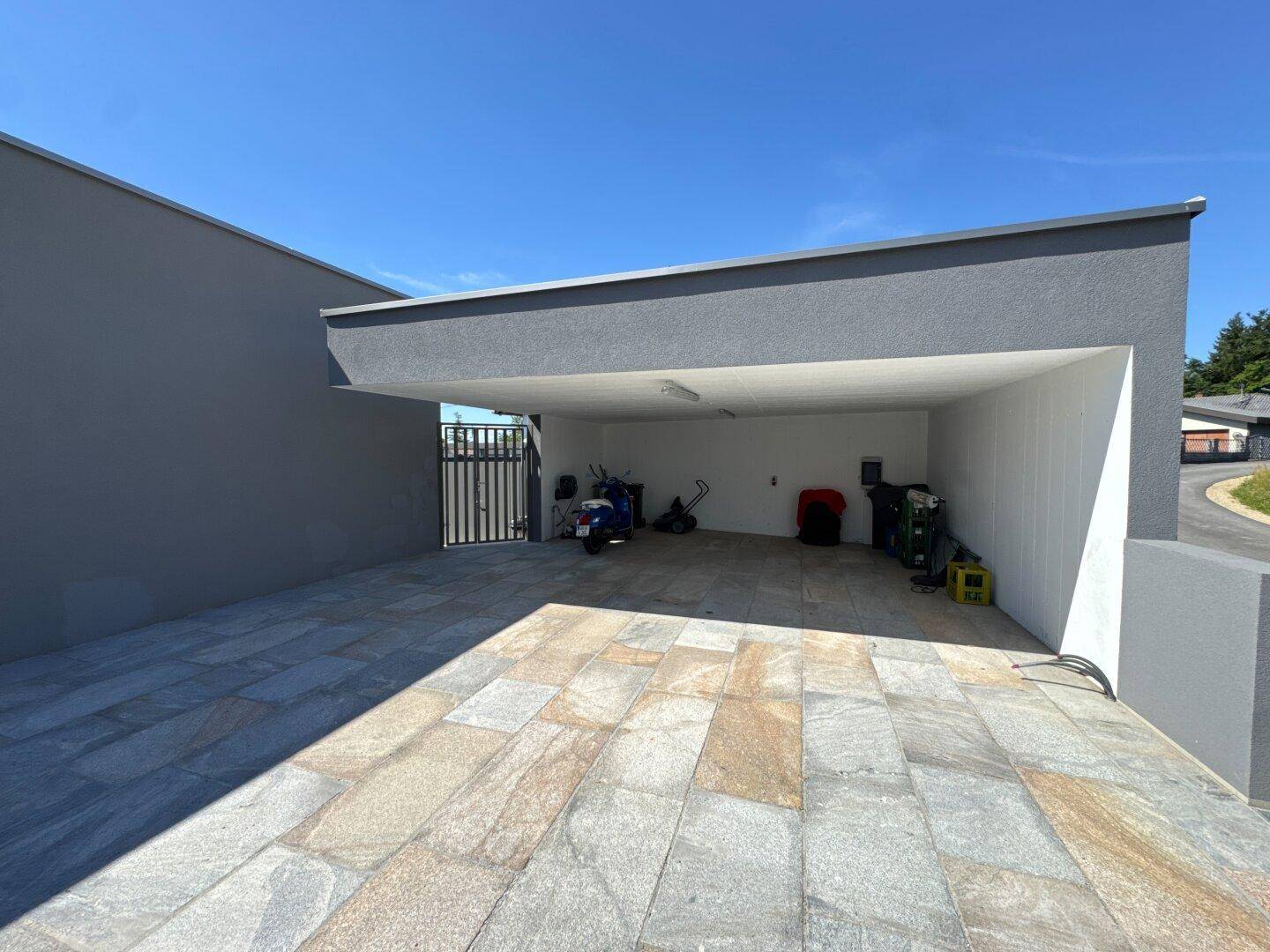 Geräumiger Carport mit gepflastertem Boden, bietet geschützten Stellplatz für Fahrzeuge und Geräte.