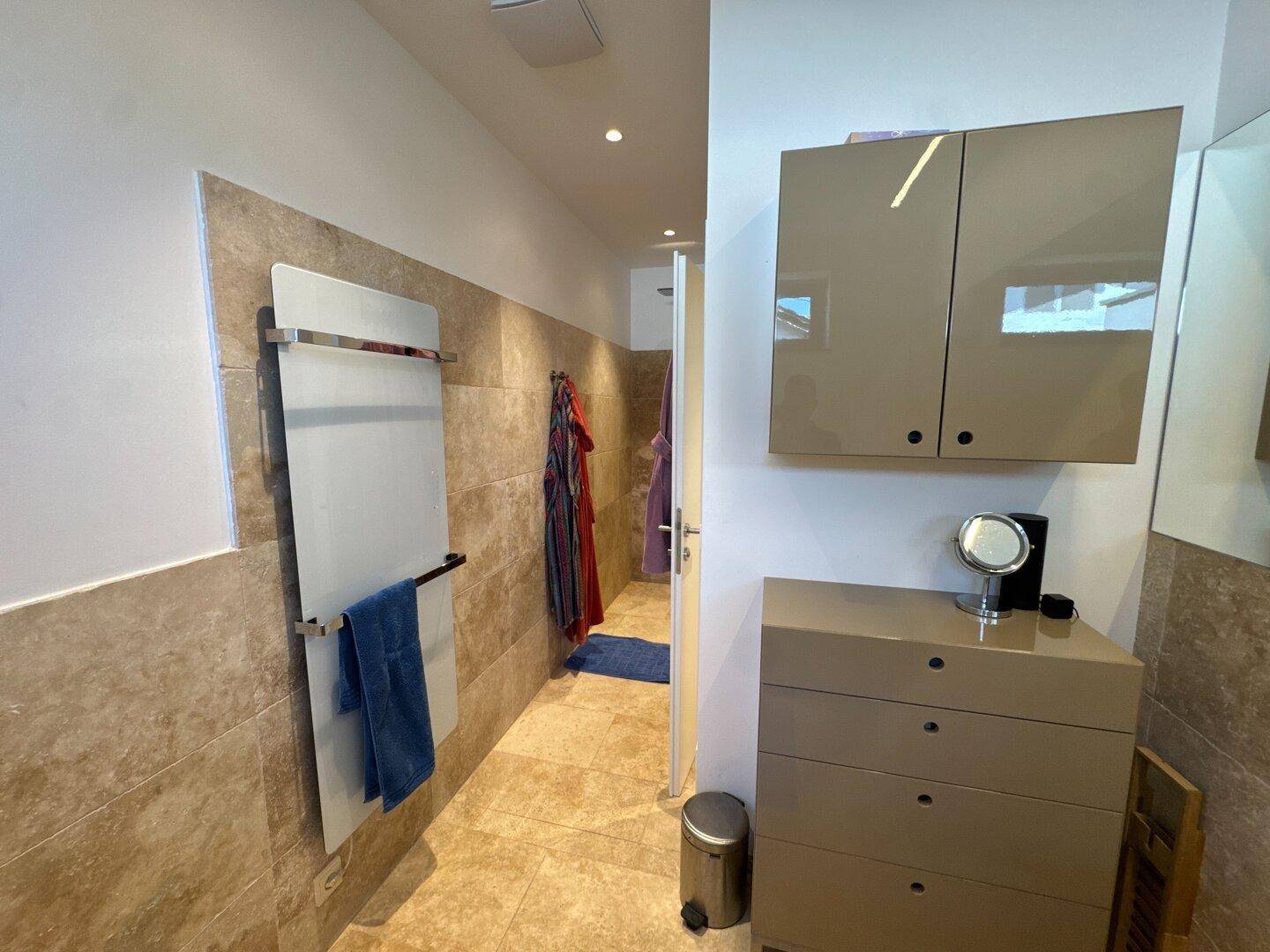 Modernes Badezimmer mit Fliesenboden, beheiztem Handtuchhalter und Spiegelschrank.