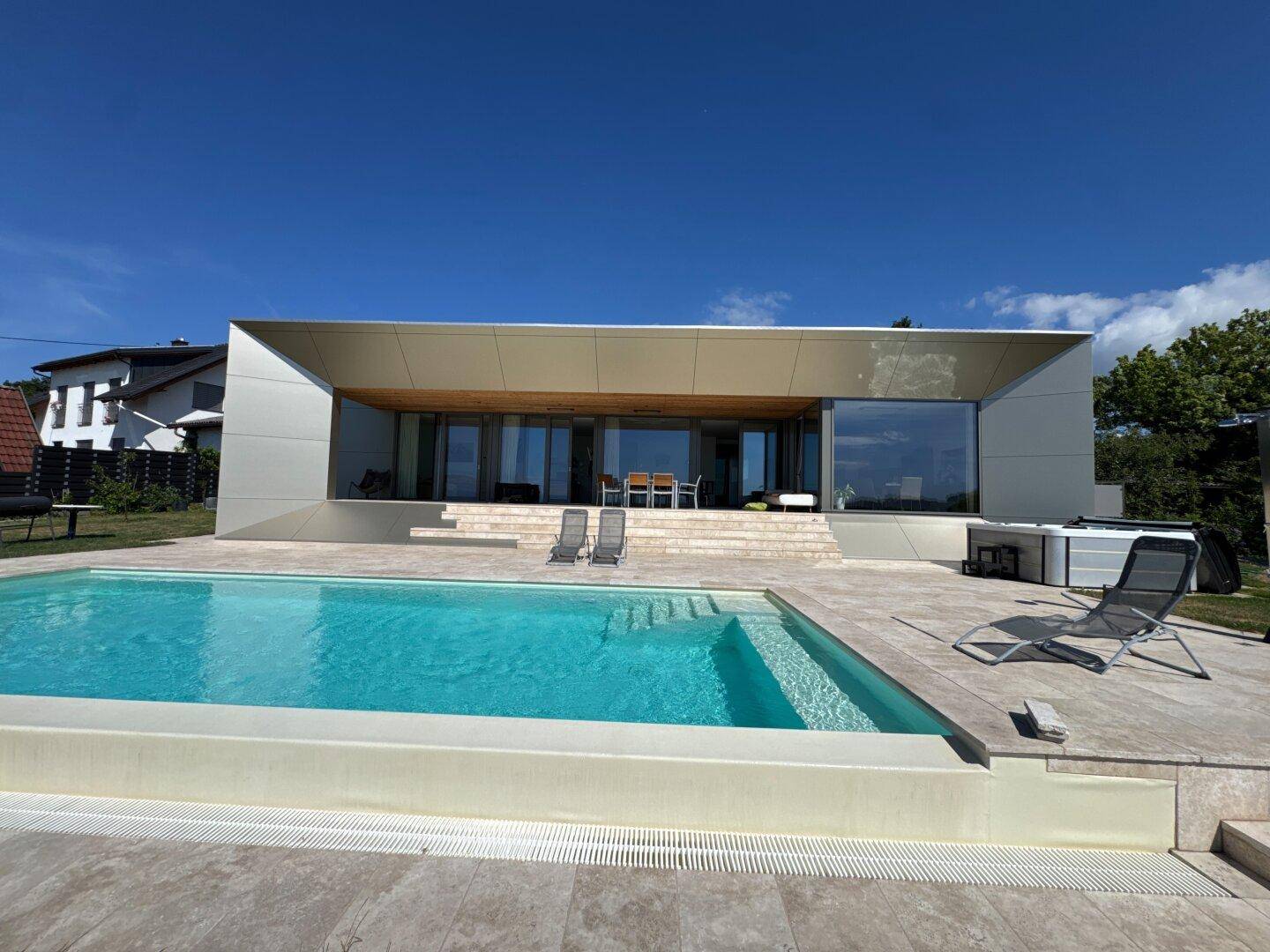 Zeitgenössische Villa mit großem Poolbereich und weitläufiger Terrasse unter blauem Himmel.