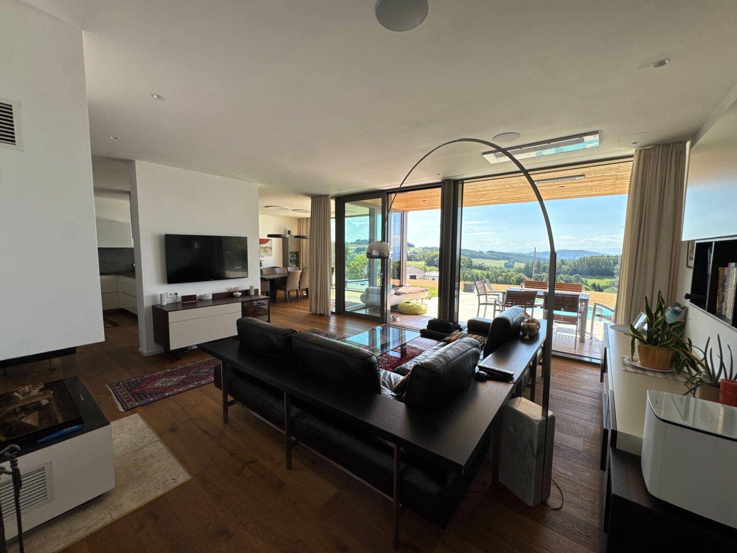 Lichtdurchflutetes Wohnzimmer mit großen Fensterfronten, Holzboden und Panoramablick auf die Landschaft.