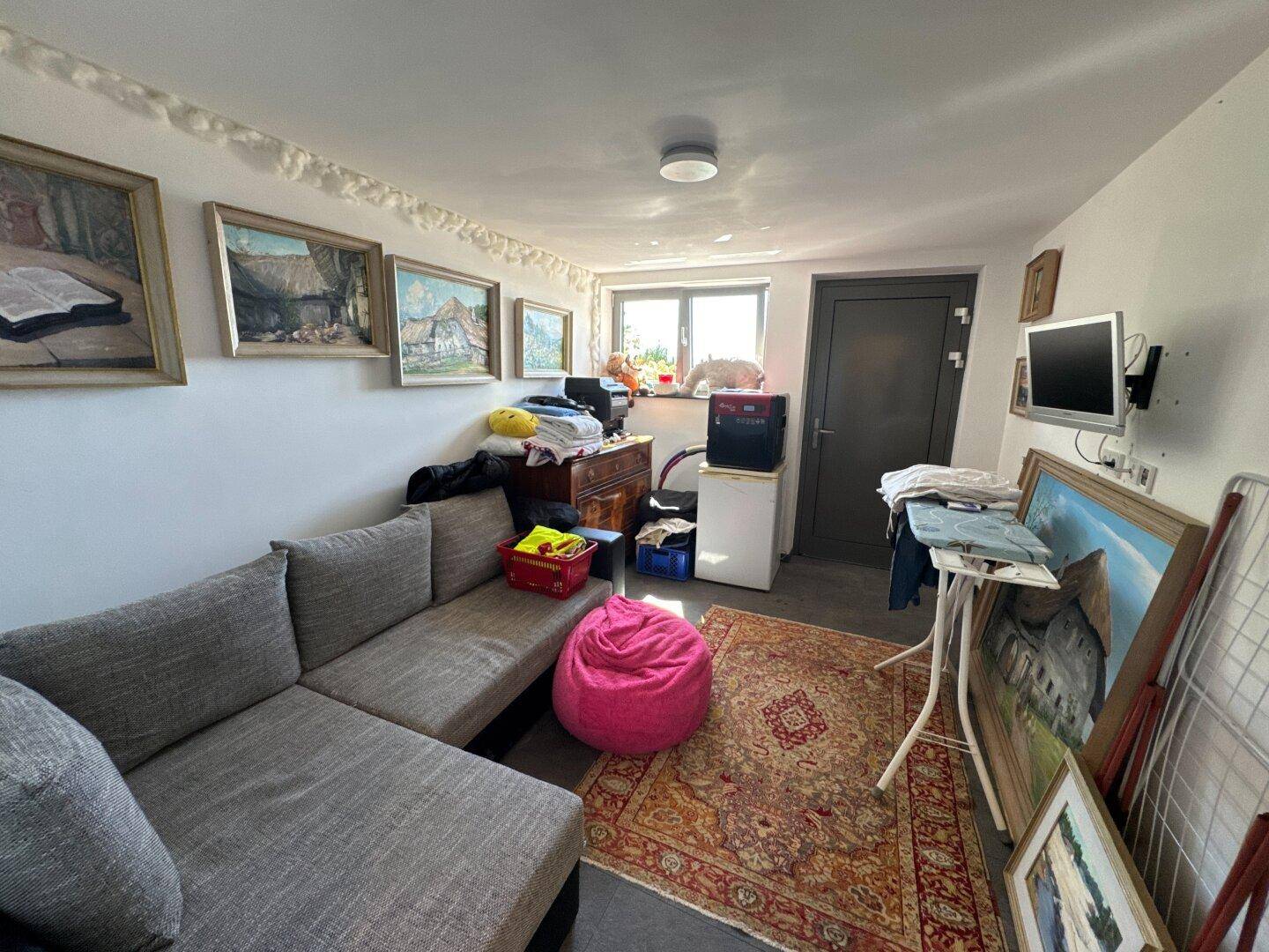 Vielseitiger Raum mit Sofa, Fenster und Bildern, ideal als Hobby- oder Gästezimmer nutzbar.