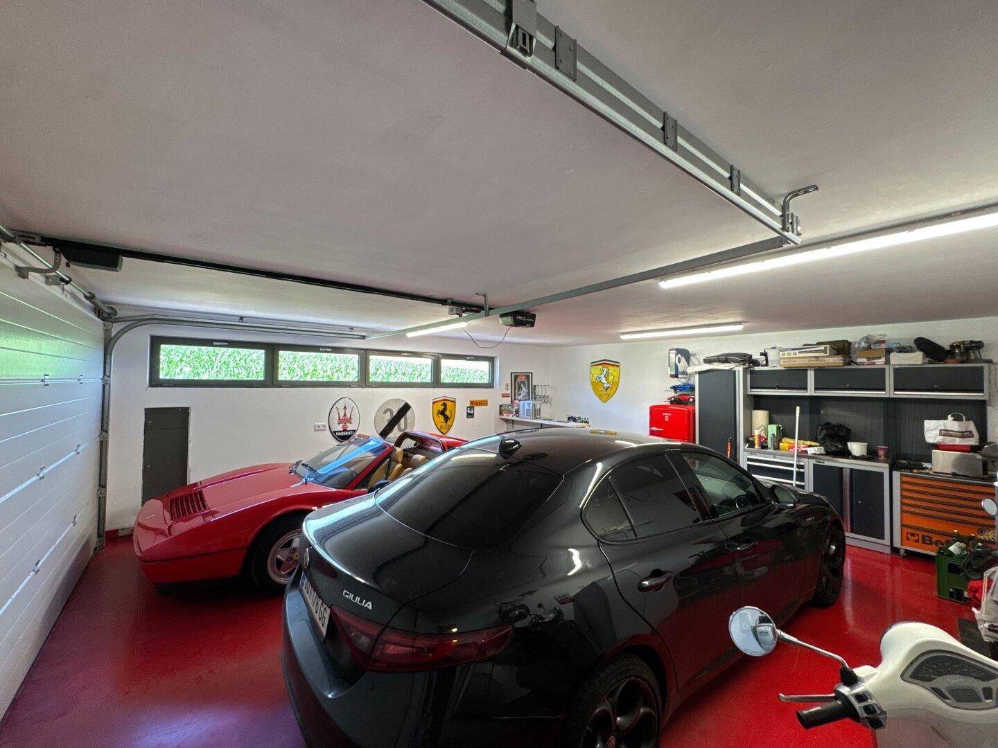 Geräumige Garage mit rotem Boden, bietet Platz für mehrere Fahrzeuge und Werkstattausrüstung.