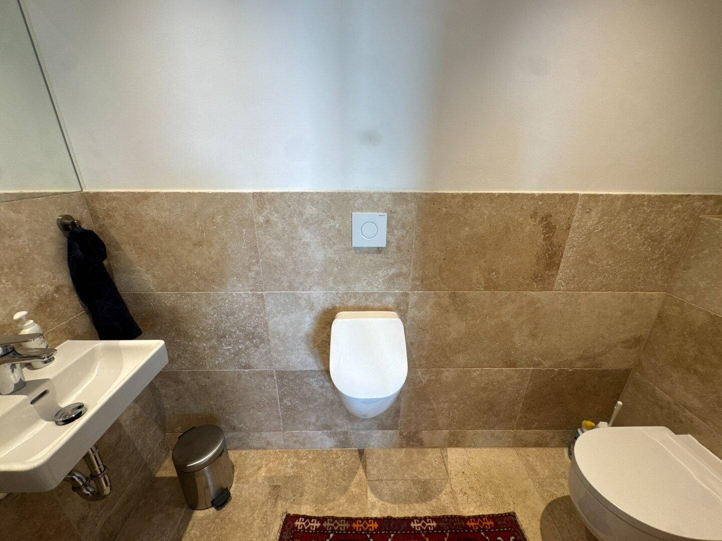 Modernes Gäste-WC mit Wand-WC, kleinem Waschbecken und Fliesen an Wänden und Boden.