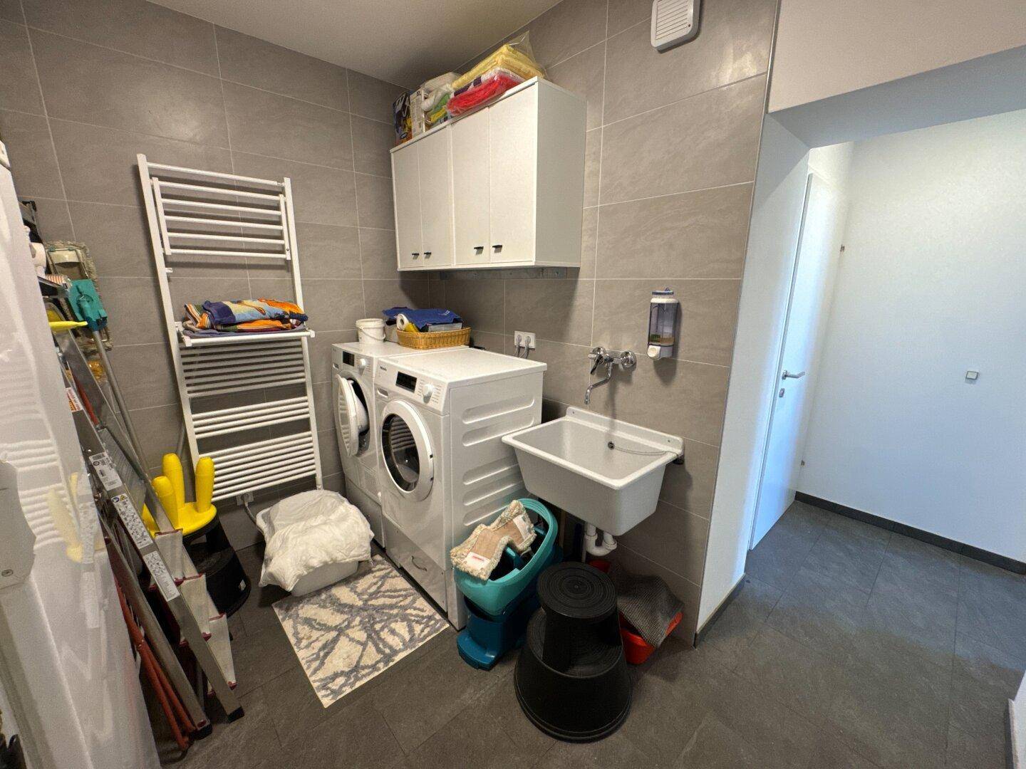 Praktischer Hauswirtschaftsraum mit Waschmaschine, Trockner und Waschbecken, ausgestattet mit Fliesenboden.
