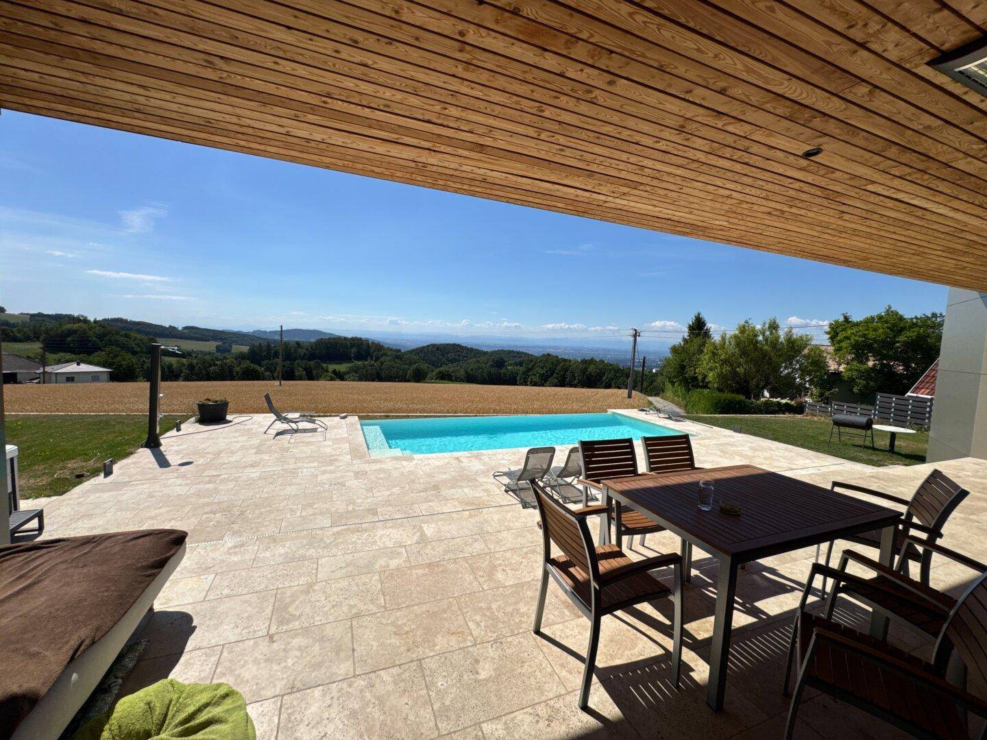 Überdachte Terrasse mit Essbereich und Liegestühlen, bietet einen herrlichen Blick auf den Pool und die Landschaft.