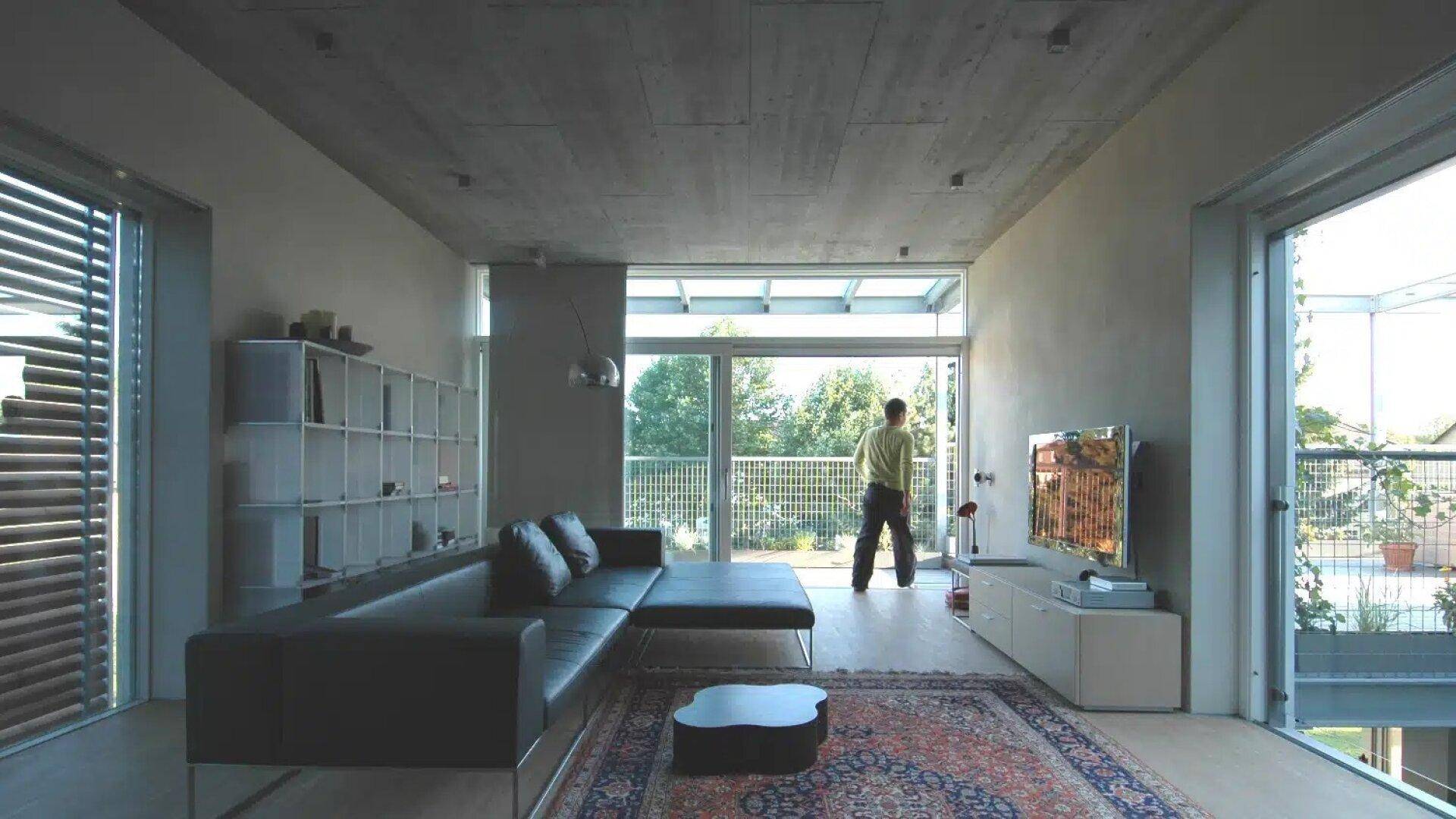Modernes Wohnzimmer mit großer Fensterfront, Ledersofa und Blick ins Grüne.