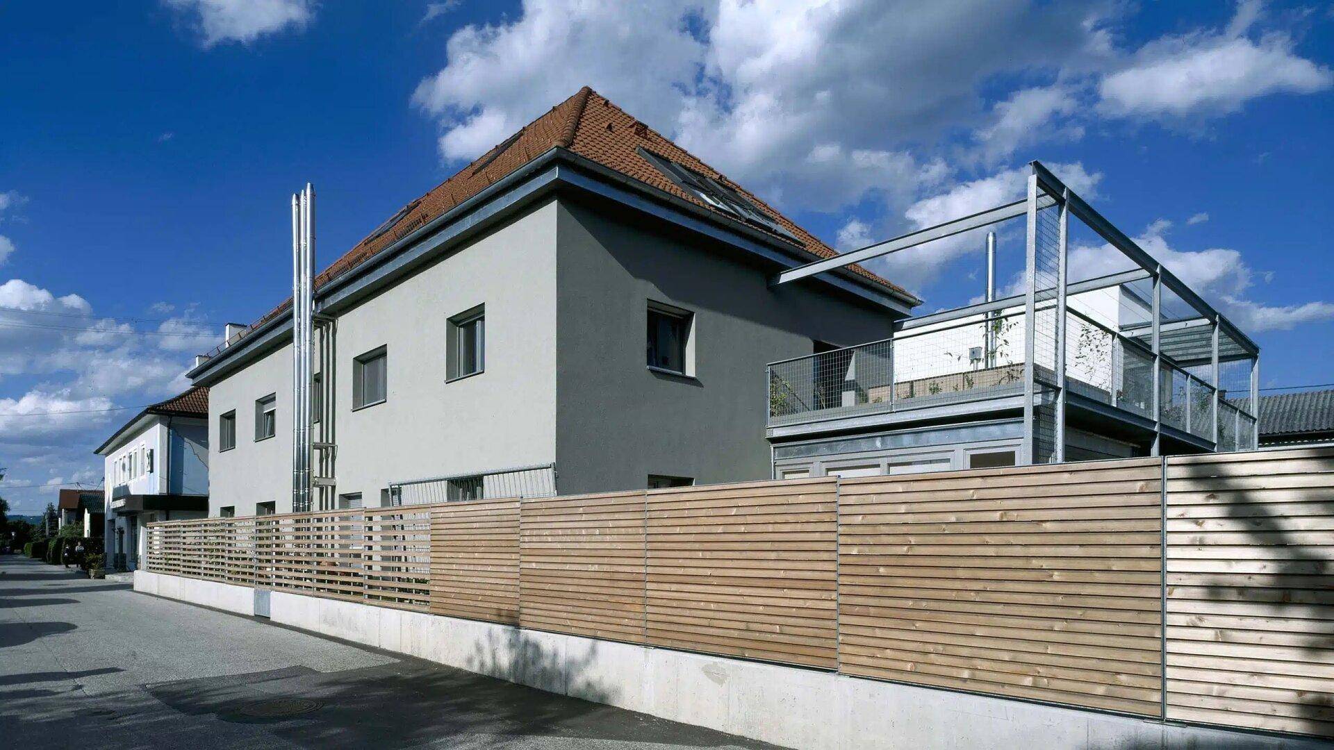 Seitenansicht des Hauses mit Holzzaun, Balkon und moderner Architektur.
