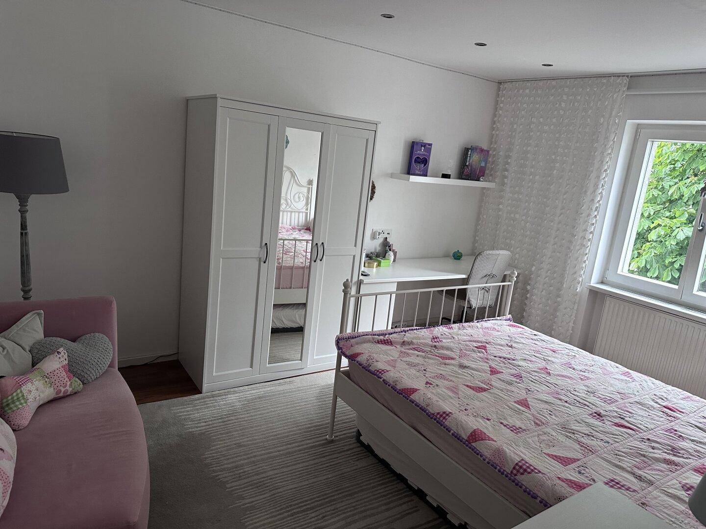 Helles Kinderzimmer mit Einzelbett, weißem Kleiderschrank und Schreibtisch am Fenster.