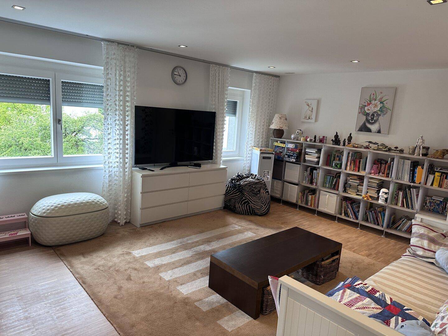 Gemütliches Wohnzimmer mit großem Fernseher, Bücherregalen und Teppichboden.