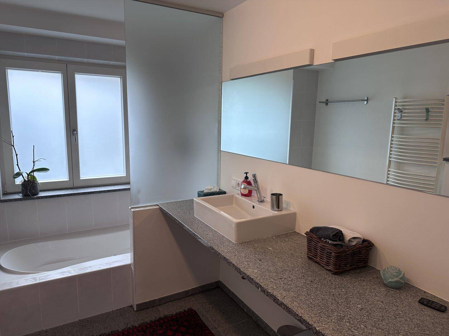 Modernes Badezimmer mit Badewanne, Einzelwaschbecken und großem Spiegel.