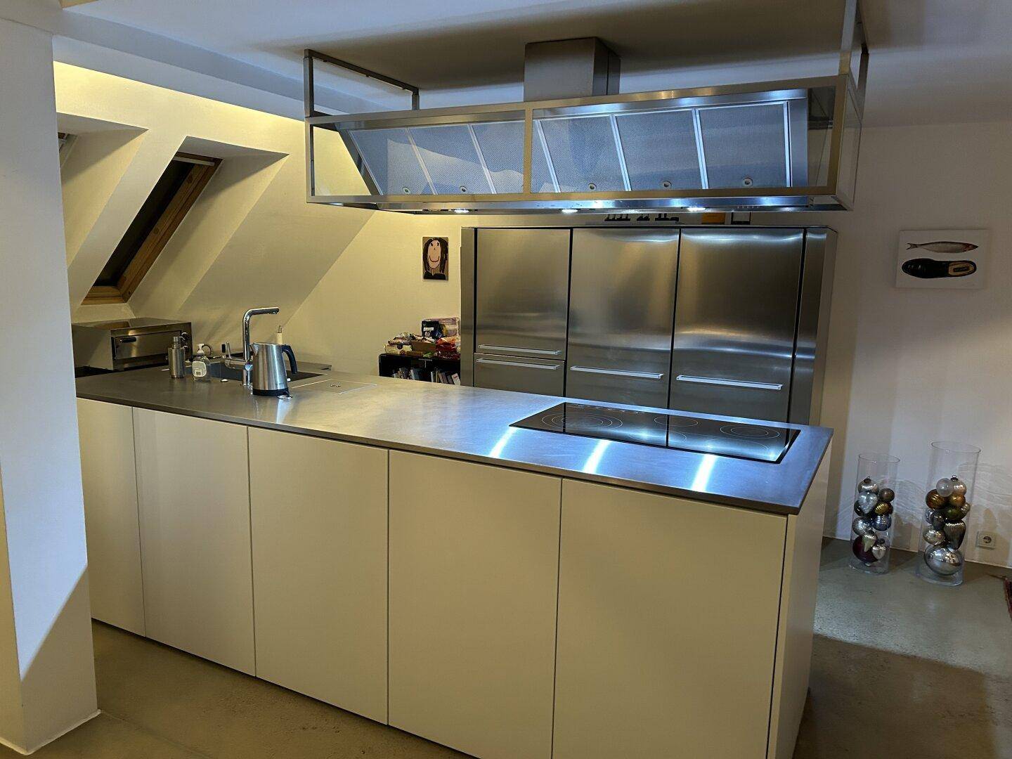 Moderne Küche mit Edelstahlgeräten, Kochinsel und Dachfenstern.