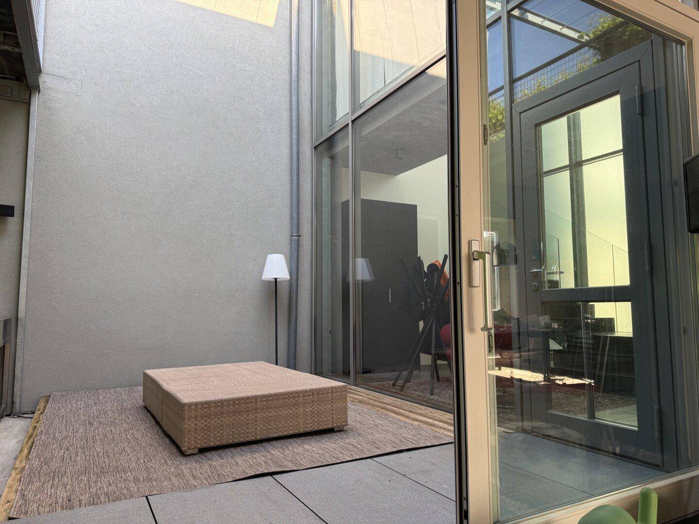 Geschützter Terrassenbereich mit Sitzgelegenheit und Zugang zum Innenbereich durch Glasfront.