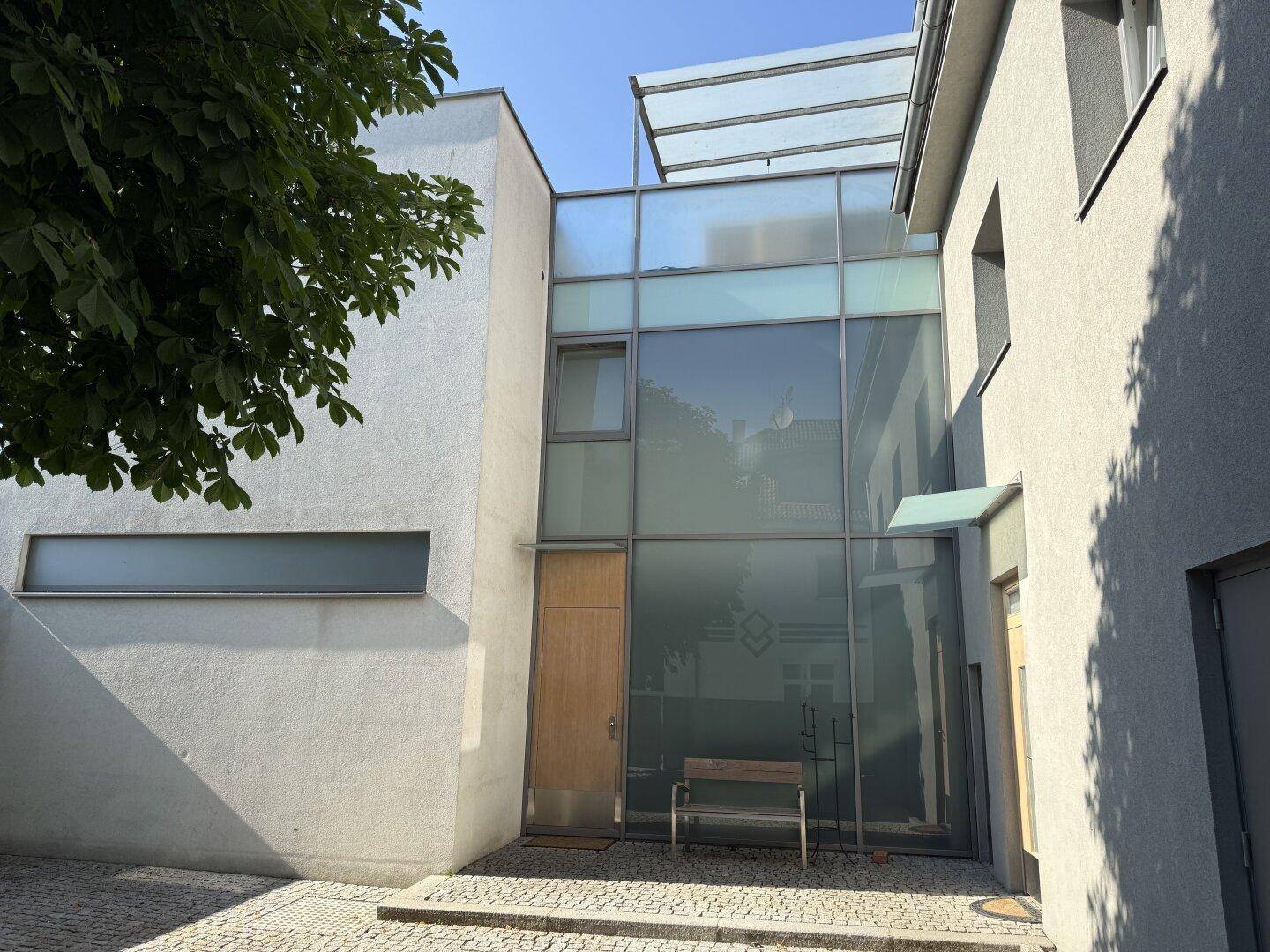 Moderne Gebäudefassade mit großen Glasflächen und minimalistischem Design am Eingangsbereich.