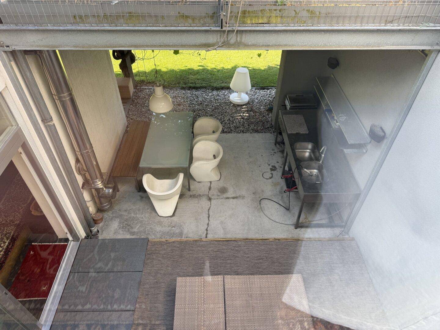 Blick von oben auf die überdachte Terrasse mit Essbereich und Außenküche im Grünen.