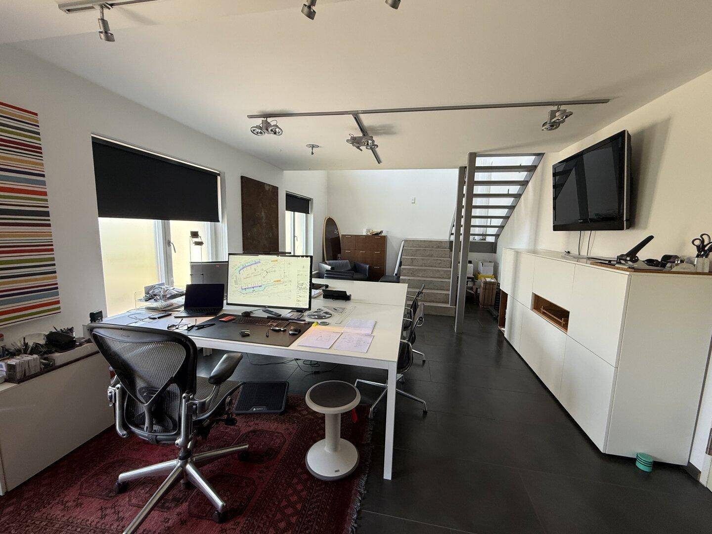Geräumiges Büro mit großem Schreibtisch, dunklem Fliesenboden und offener Treppe im Hintergrund.