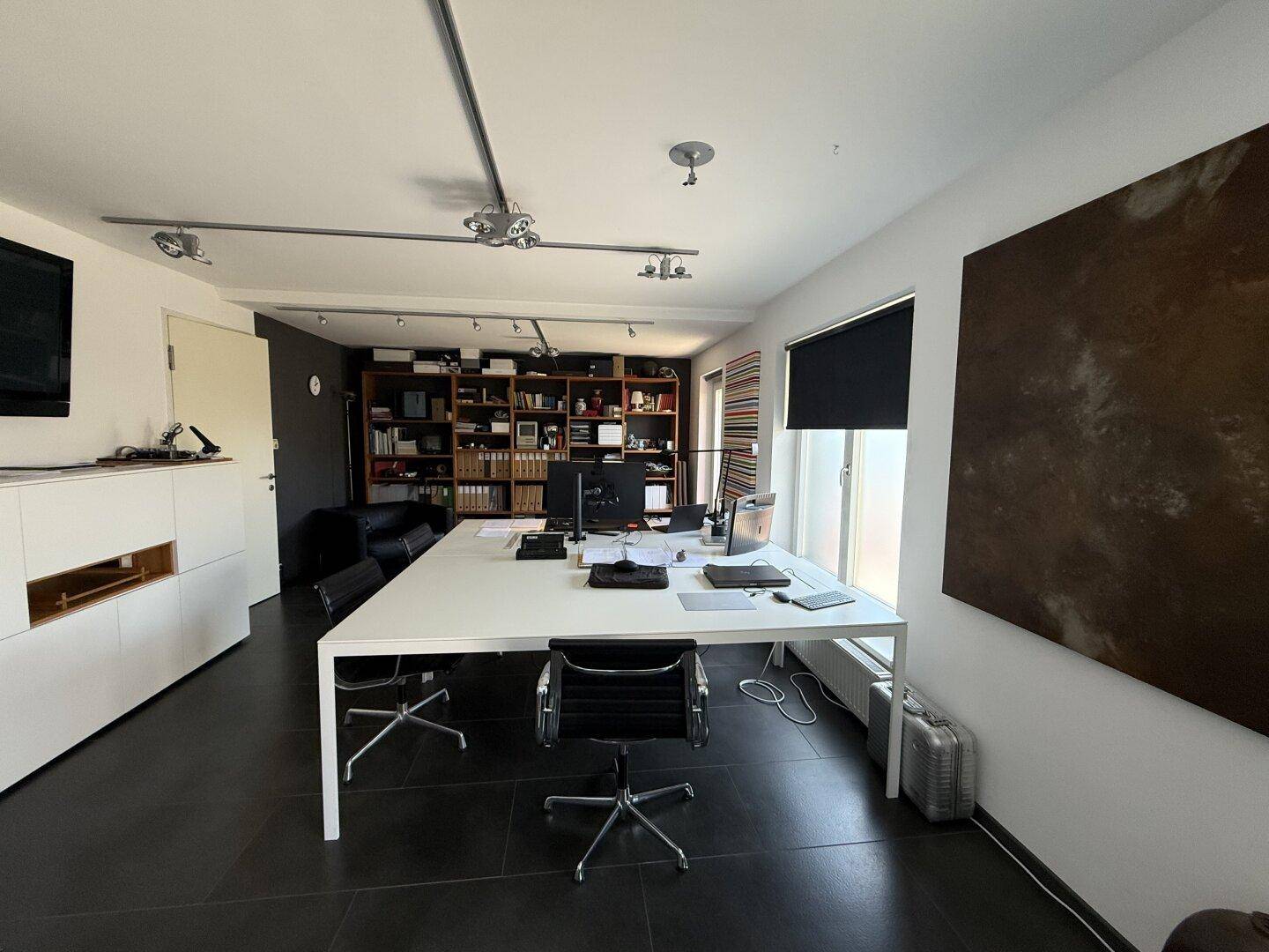Helles Büro mit umfangreichem Bücherregal, großem Schreibtisch und dunklem Fliesenboden.
