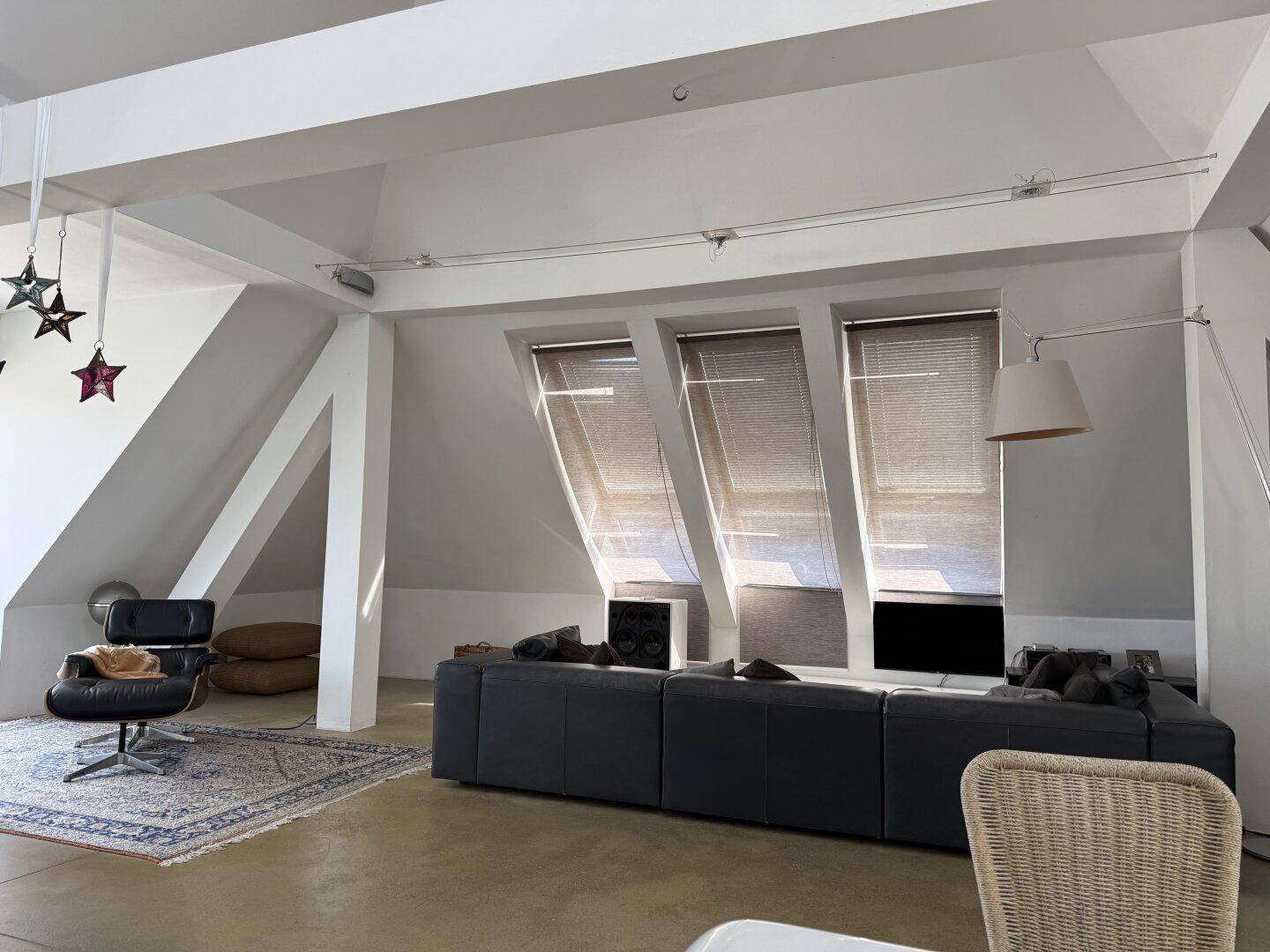 Geräumiges Wohnzimmer mit schrägen Decken, Dachfenstern und großem, modernem Sofa.