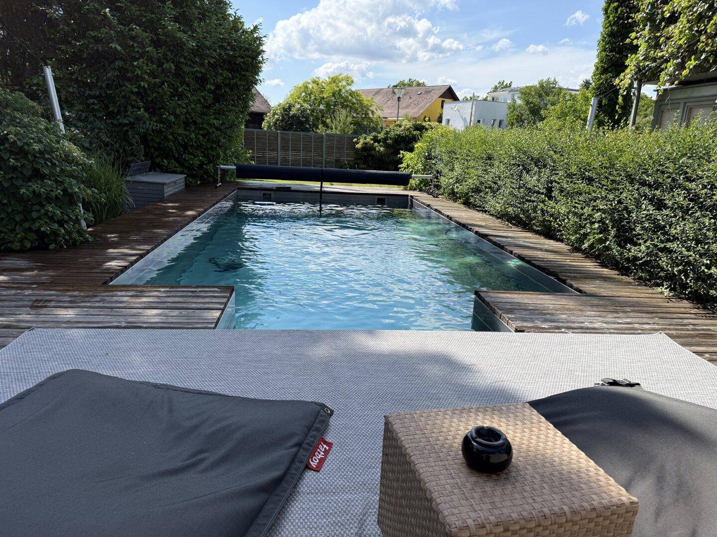 Entspannungsbereich am Pool mit bequemen Liegekissen und Holzdielen.
