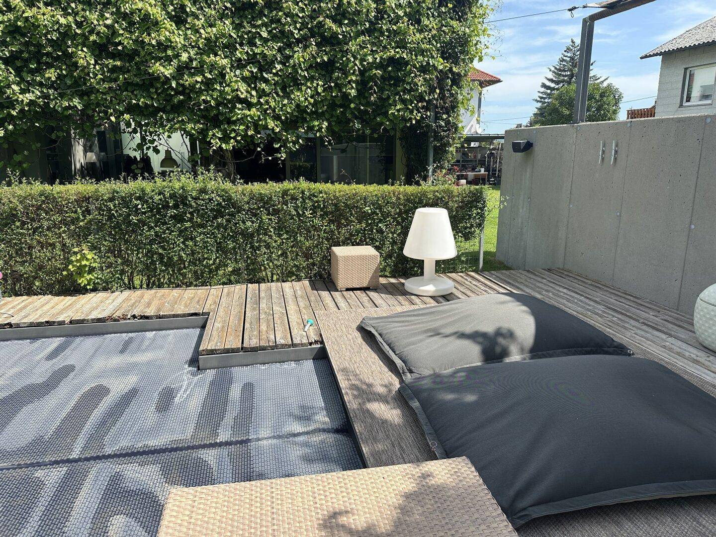 Außenbereich mit Holzdeck, bequemen Lounge-Kissen und einem Pool mit Abdeckung.