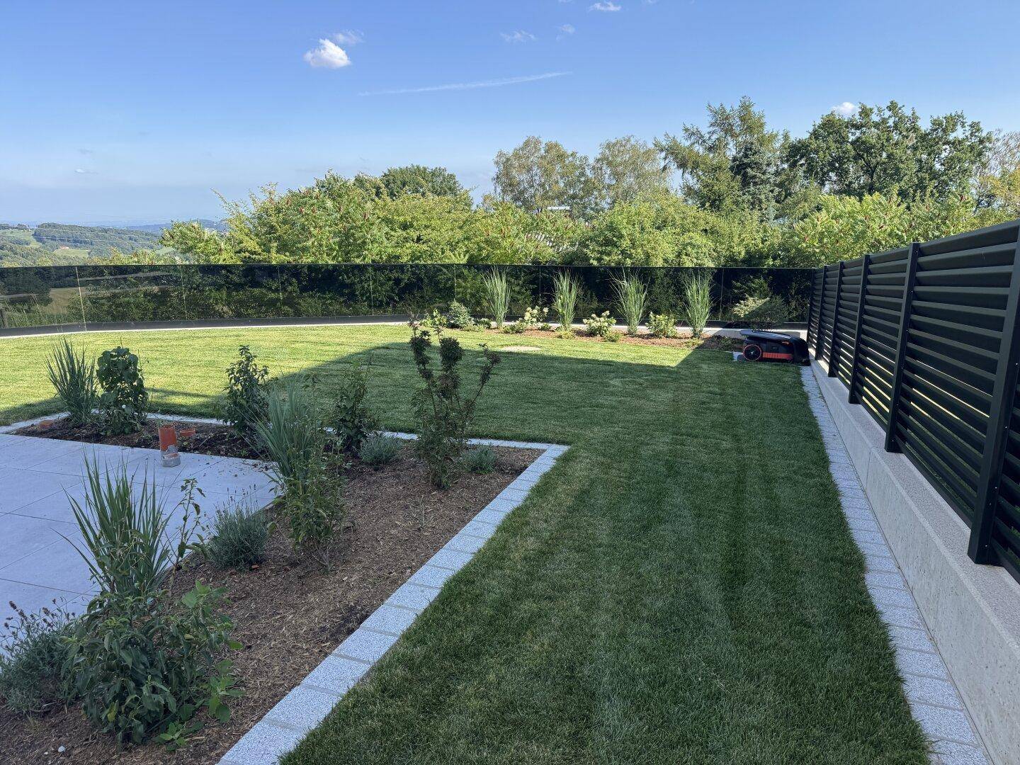Gepflegter Gartenbereich mit Rasenfläche, jungen Pflanzen und moderner Zaunanlage.