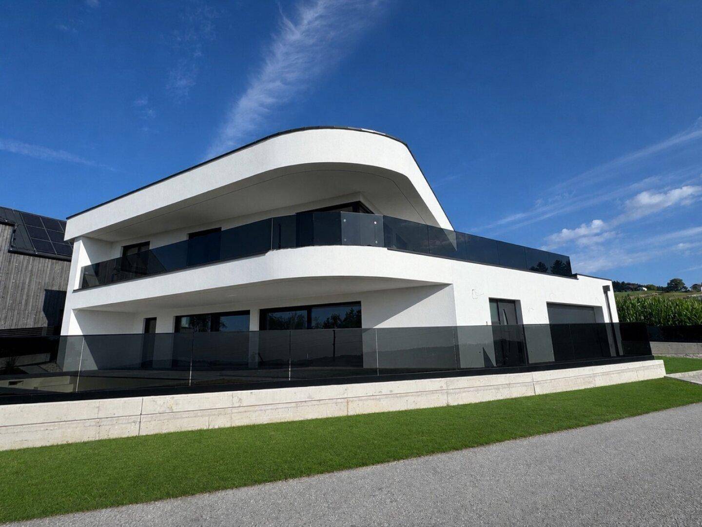 Elegante moderne Villa mit weißer Fassade, dunklen Glasgeländern und weitem Blick in die Landschaft.
