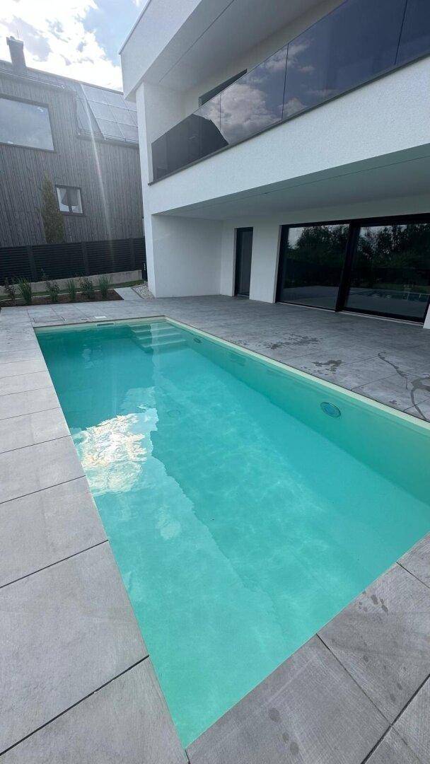 Langer, schmaler Swimmingpool umgeben von grauen Fliesen und der modernen Hausfassade.
