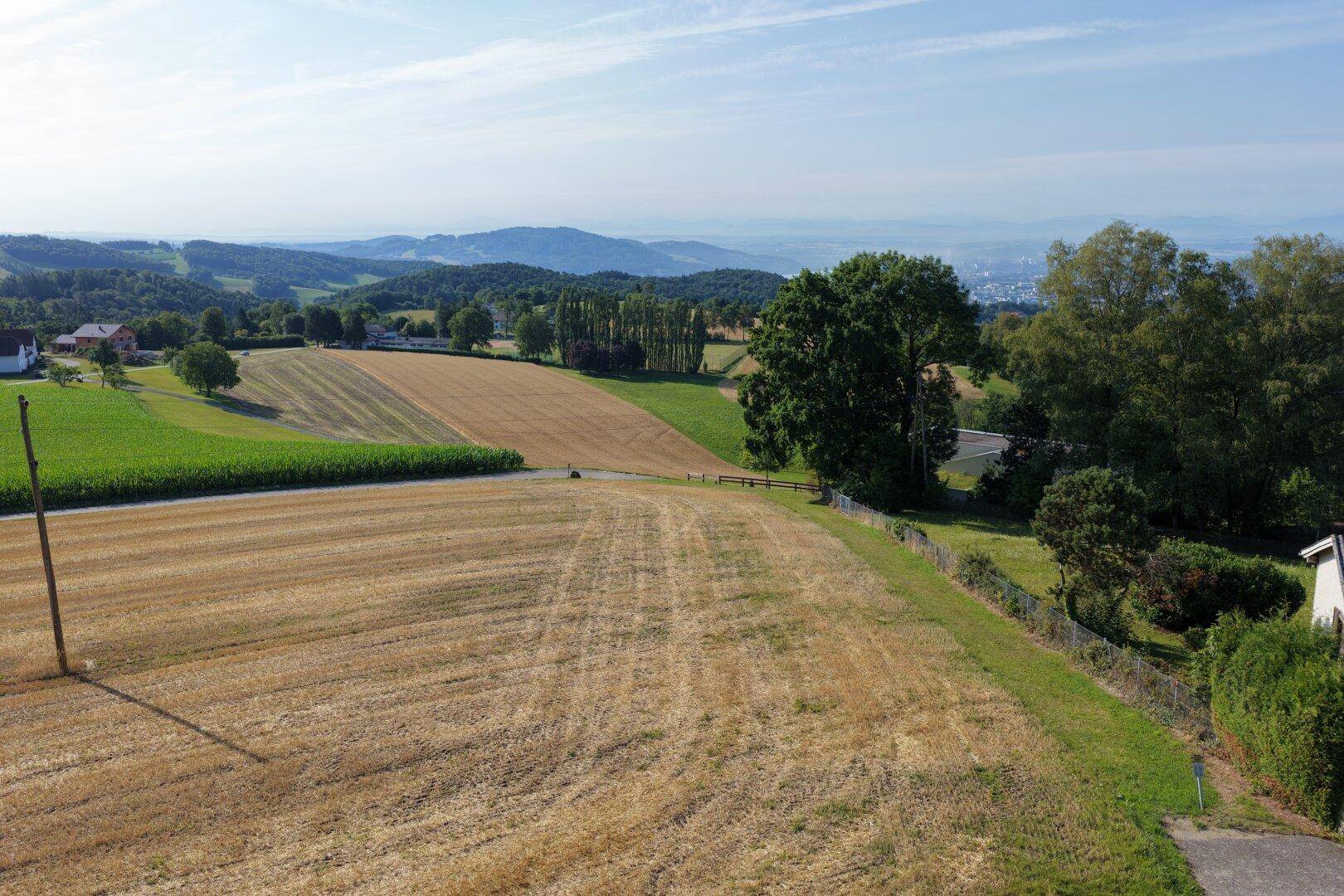 Panoramablick über weite Felder und Wälder mit einer malerischen Hügellandschaft im Hintergrund.