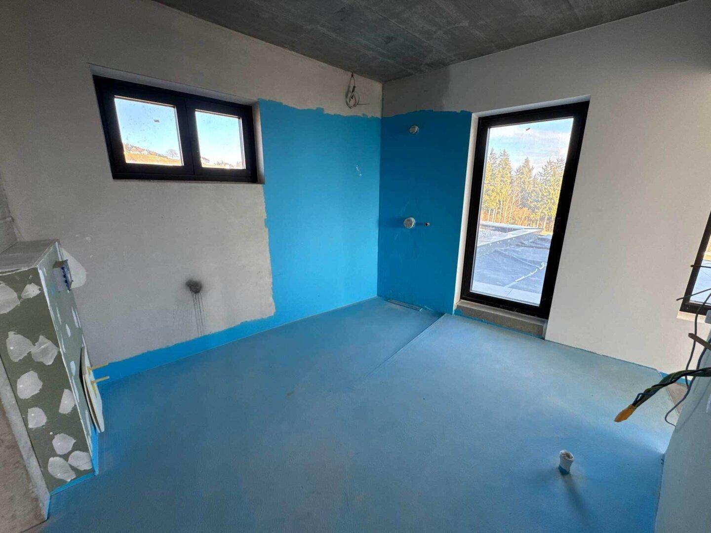 Badezimmer im Rohbau mit blauer Abdichtung, Fenster und Tür zur Außenterrasse.