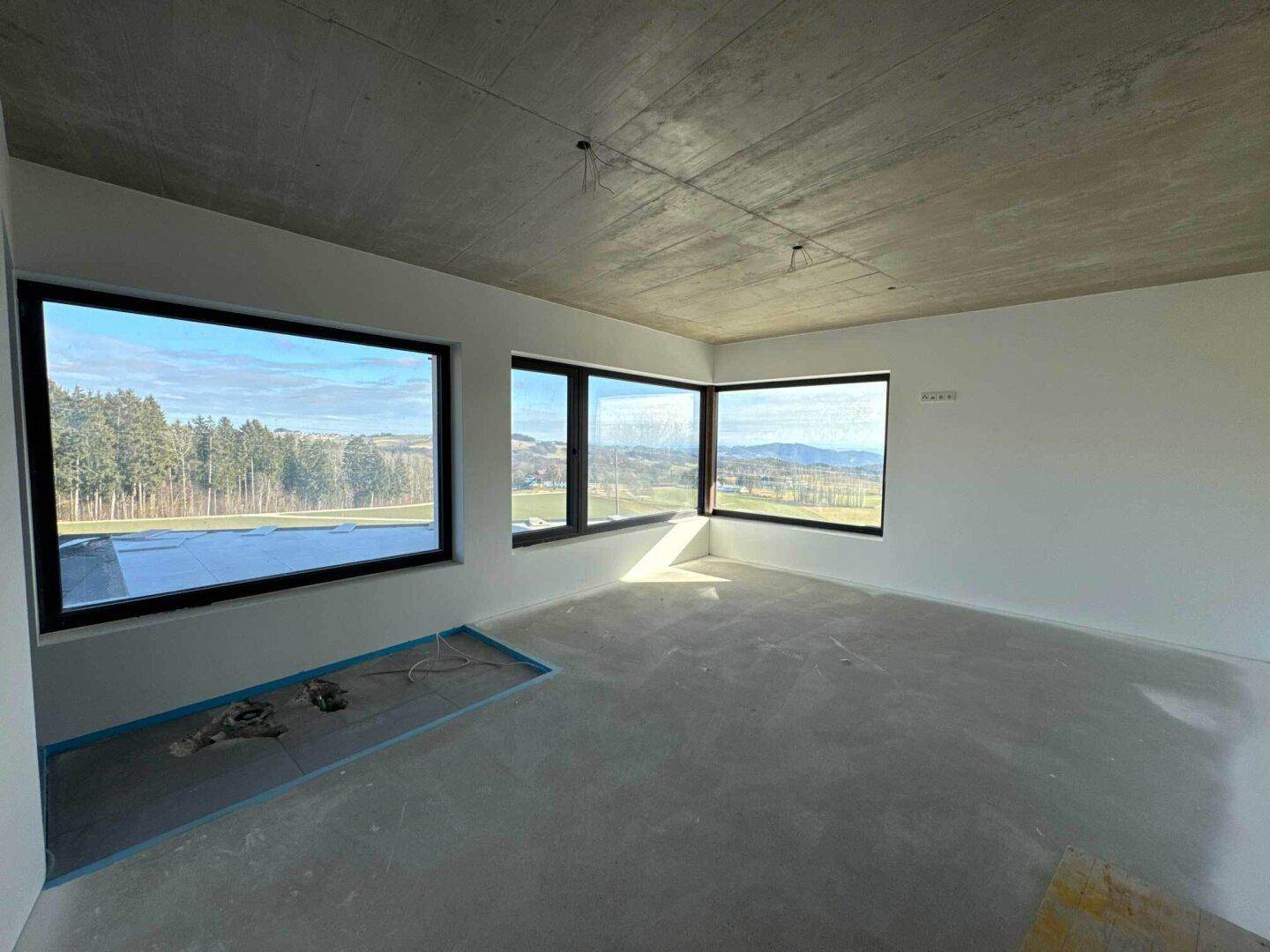 Heller Wohnraum im Rohbau mit großen Panoramafenstern und weitem Blick in die Landschaft.