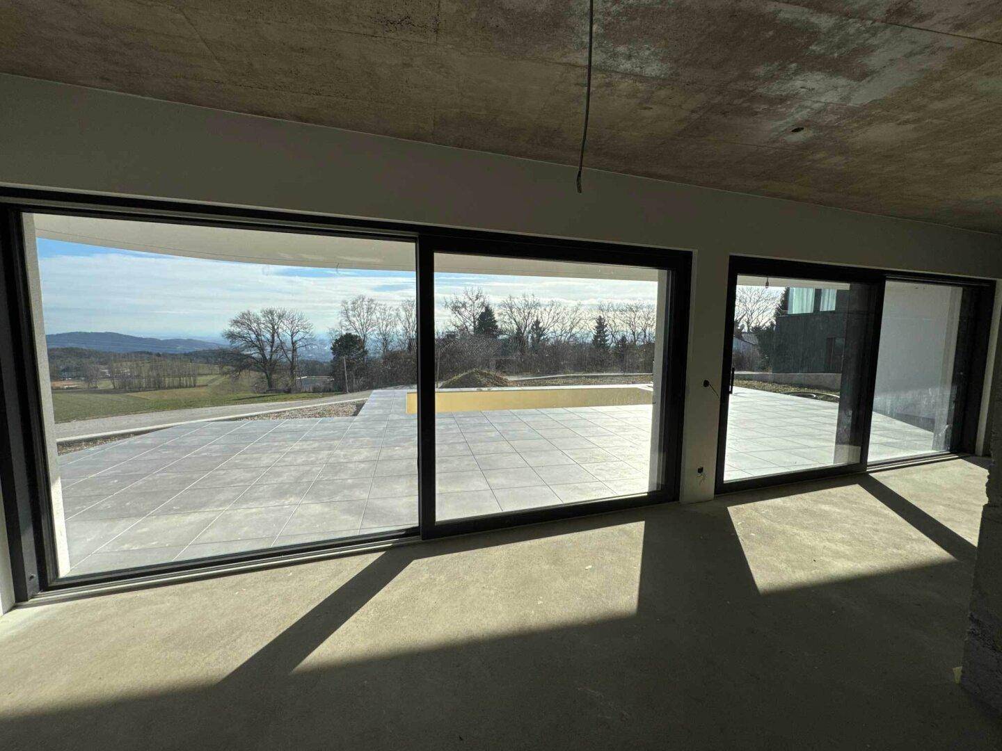 Lichtdurchfluteter Wohnraum im Rohbau mit breiten Schiebetüren und Blick auf die Terrasse.
