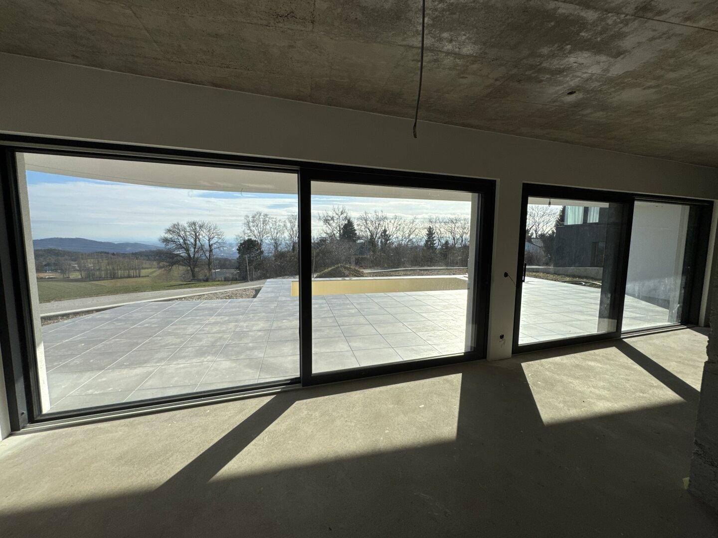 Geräumiger Wohnbereich im Rohbau mit großen Glasfronten und Zugang zur Außenterrasse.