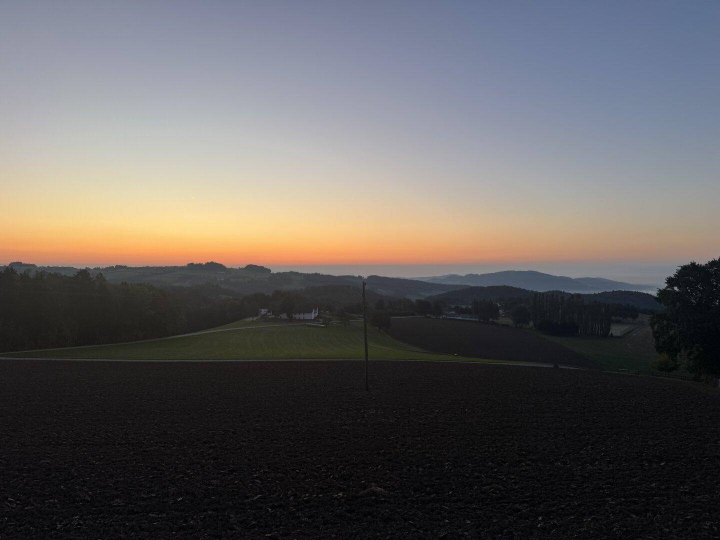 Malerischer Sonnenuntergang über einer weiten Landschaft mit Feldern und Wäldern.