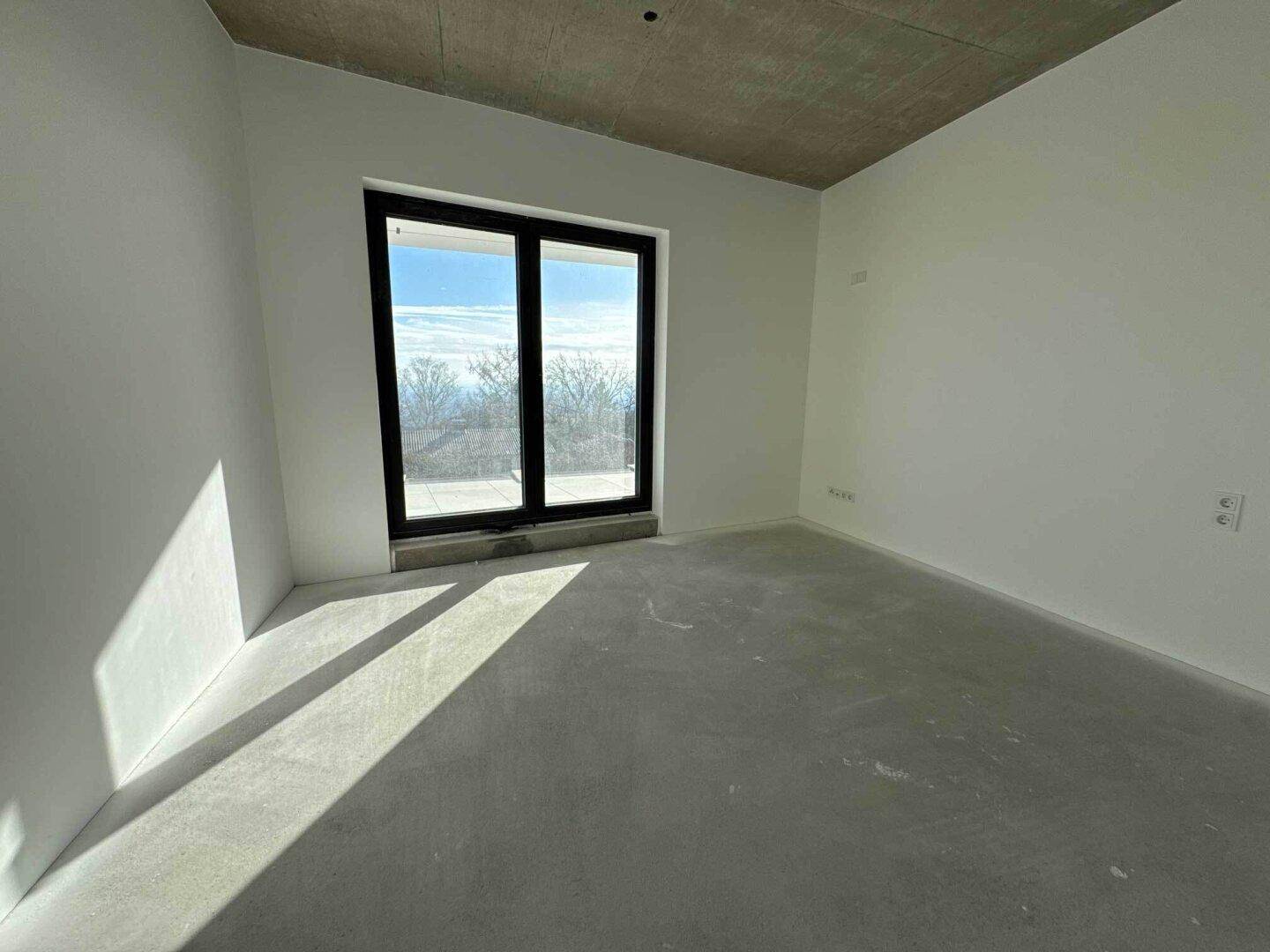 Helles Zimmer im Rohbau mit großem Fenster, geeignet als Schlaf- oder Kinderzimmer.