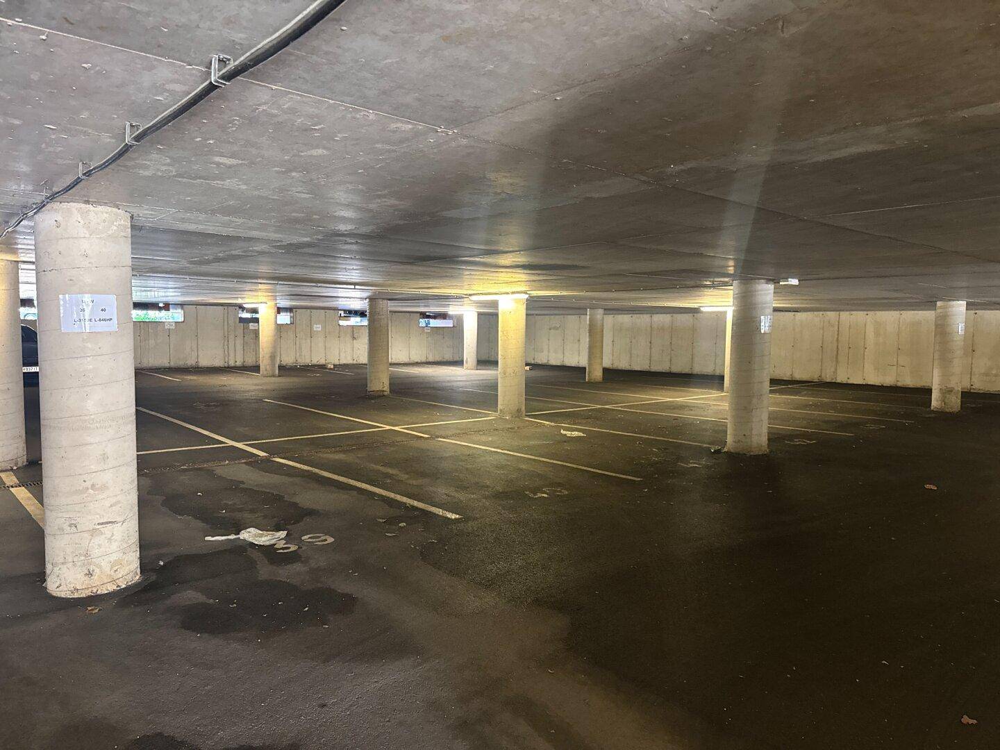 Leere Tiefgarage mit Betonpfeilern und markierten Parkplätzen, gut beleuchtet.