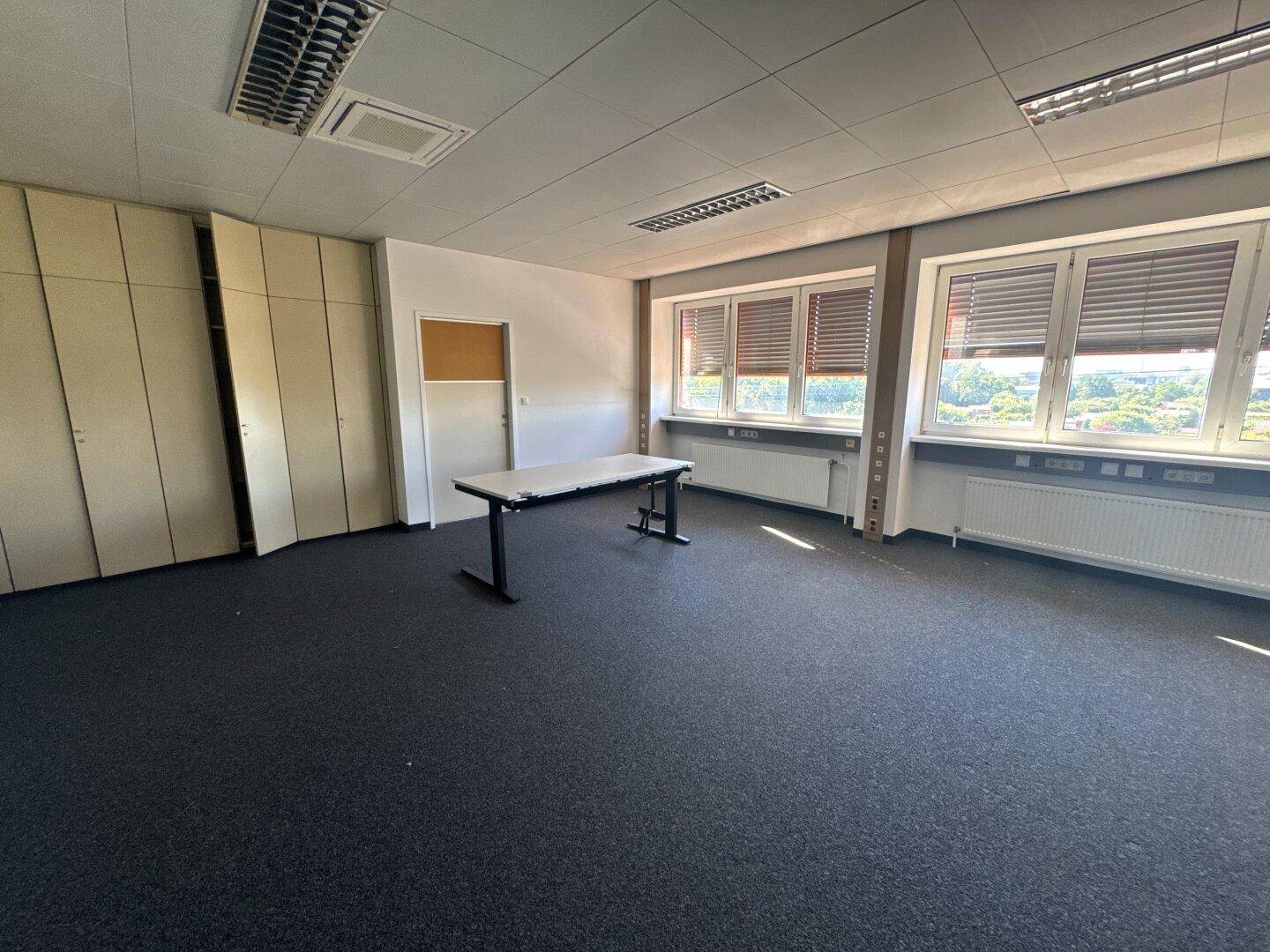 Büro mit einem Tisch, Einbauschränken und Fenstern, die viel Tageslicht hereinlassen.