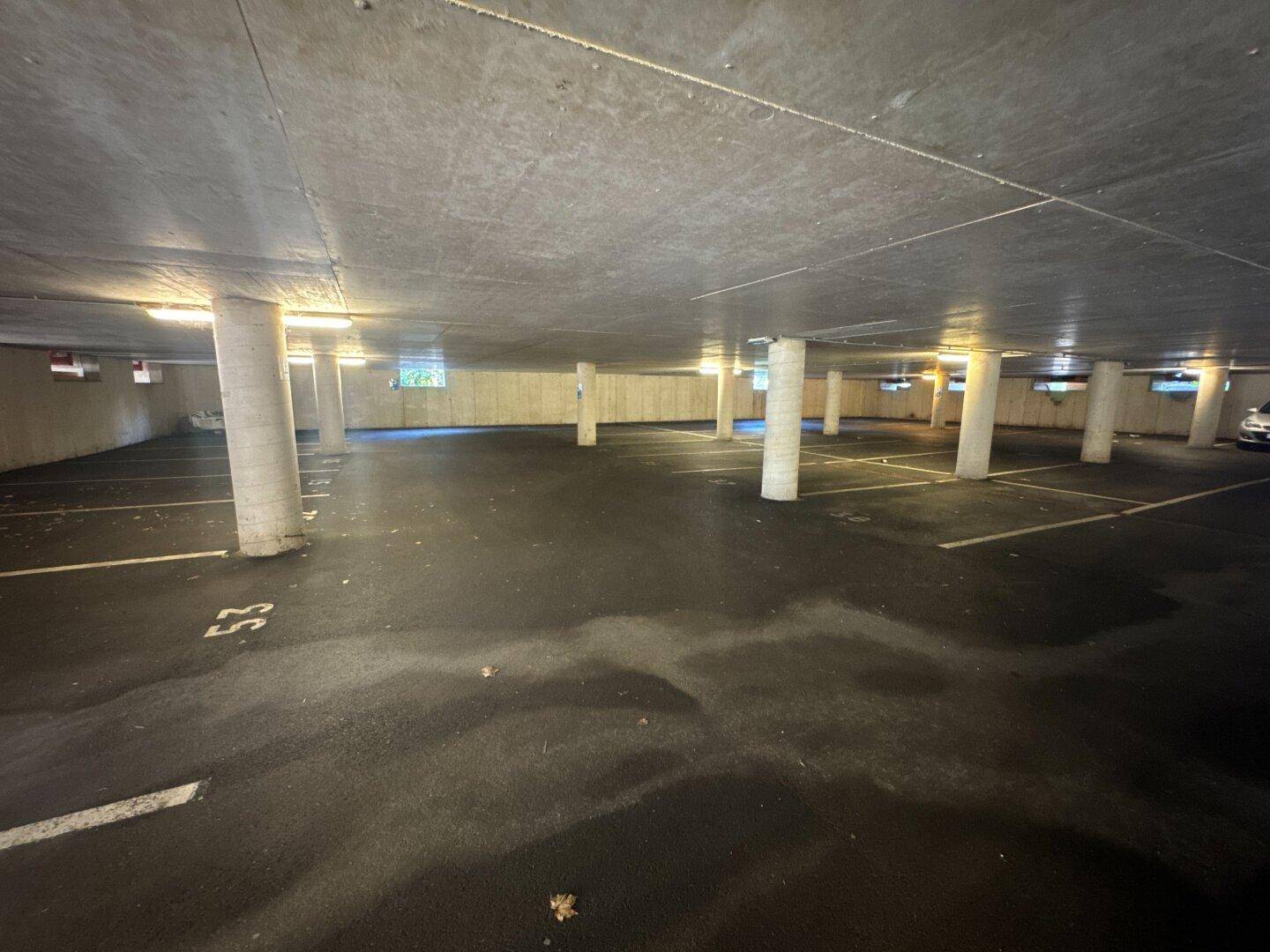 Weitläufige Tiefgarage mit Betonpfeilern und markierten Parkplätzen, gut beleuchtet.