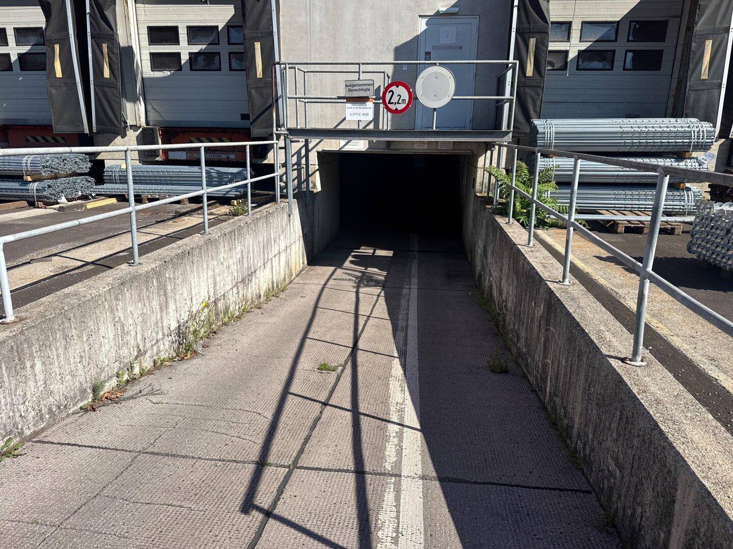 Einfahrt zu einer Tiefgarage oder Laderampe mit Höhenbegrenzung und Metallgeländern.