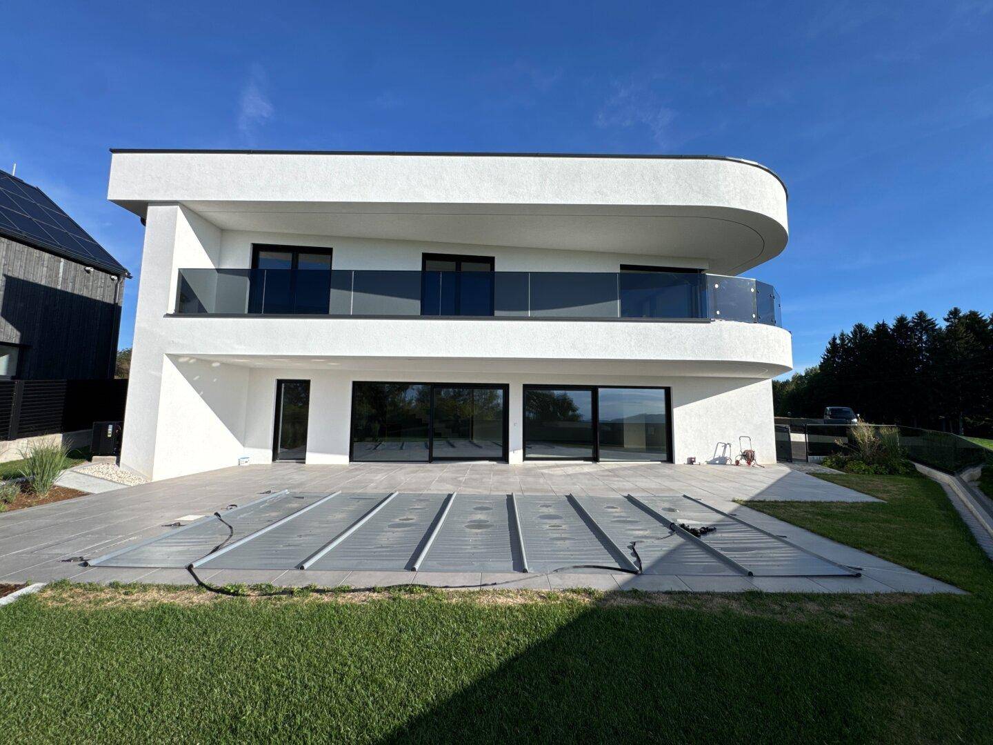 Moderne Villa mit weißer Fassade, großer Terrasse und überdachtem Poolbereich unter blauem Himmel.