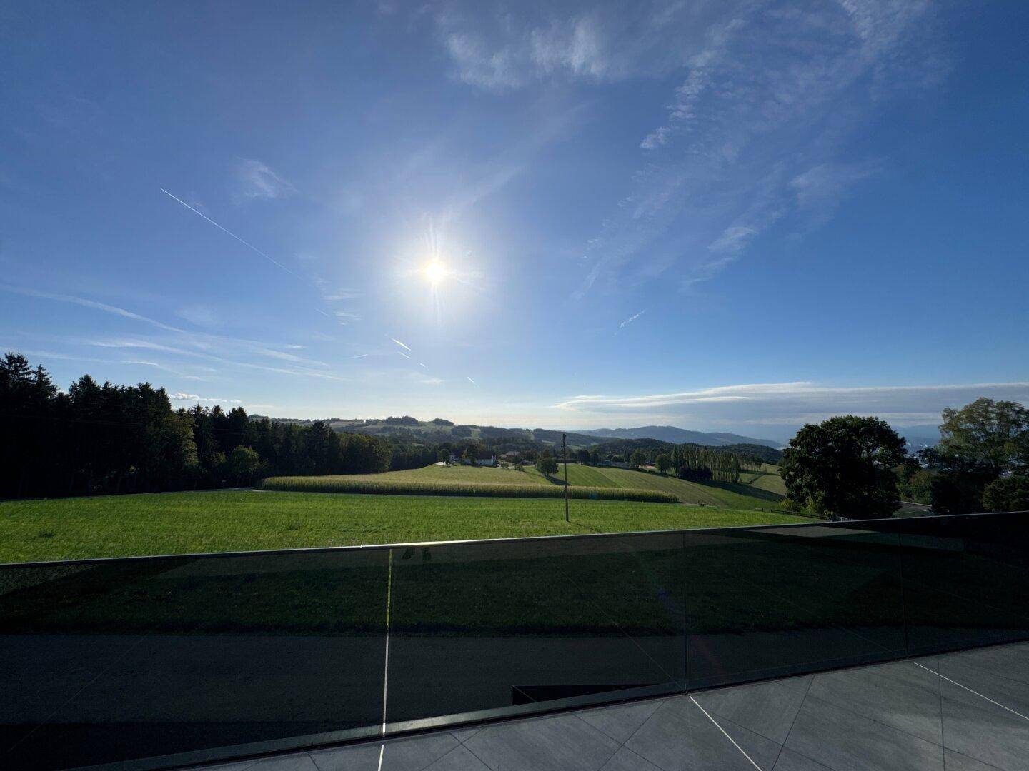 Weitläufiger Panoramablick über die grüne Landschaft und ferne Hügel unter blauem Himmel.